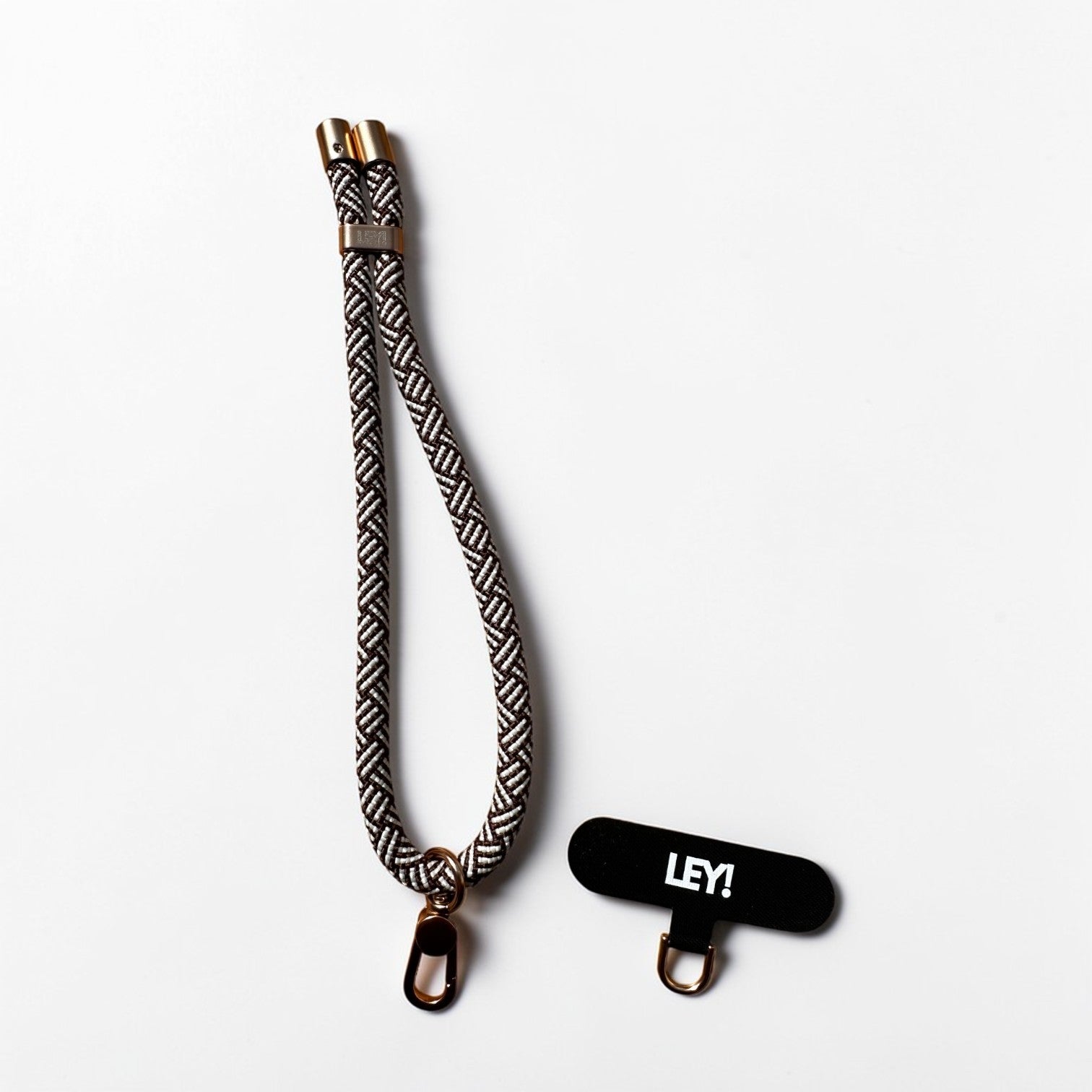 Ein gemustertes schwarz-weiß gewebtes Handy Lanyard mit Metallclips ist neben einem LEY! Schlüsselanhänger in Schwarz-Braun, der auf weißem Hintergrund abgebildet ist.