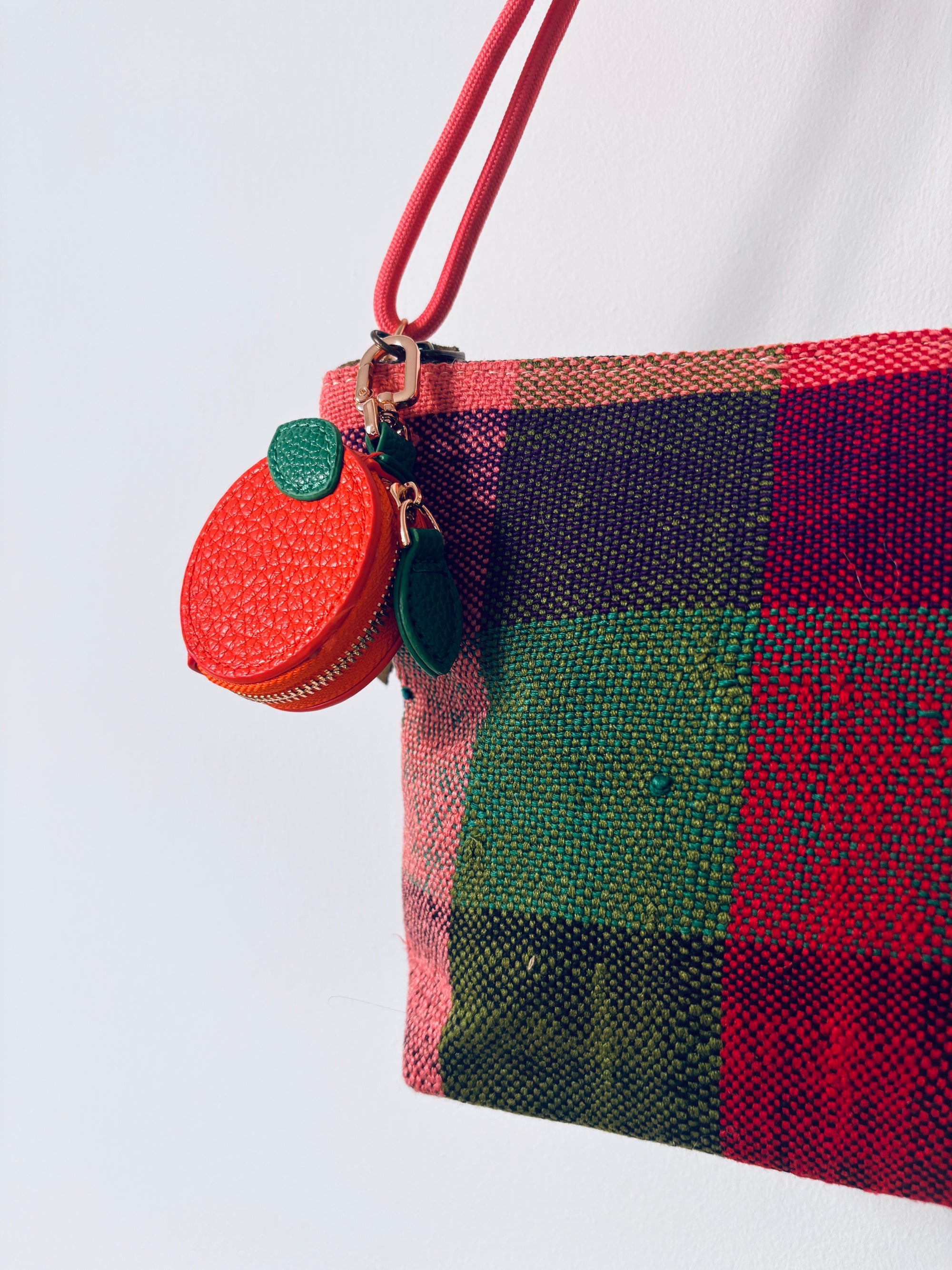 Eine bunt karierte Tasche mit einem LEY! Schlüsselanhänger - Etui - Orange und einem rot-grünen Münzbeutel am Gurt.