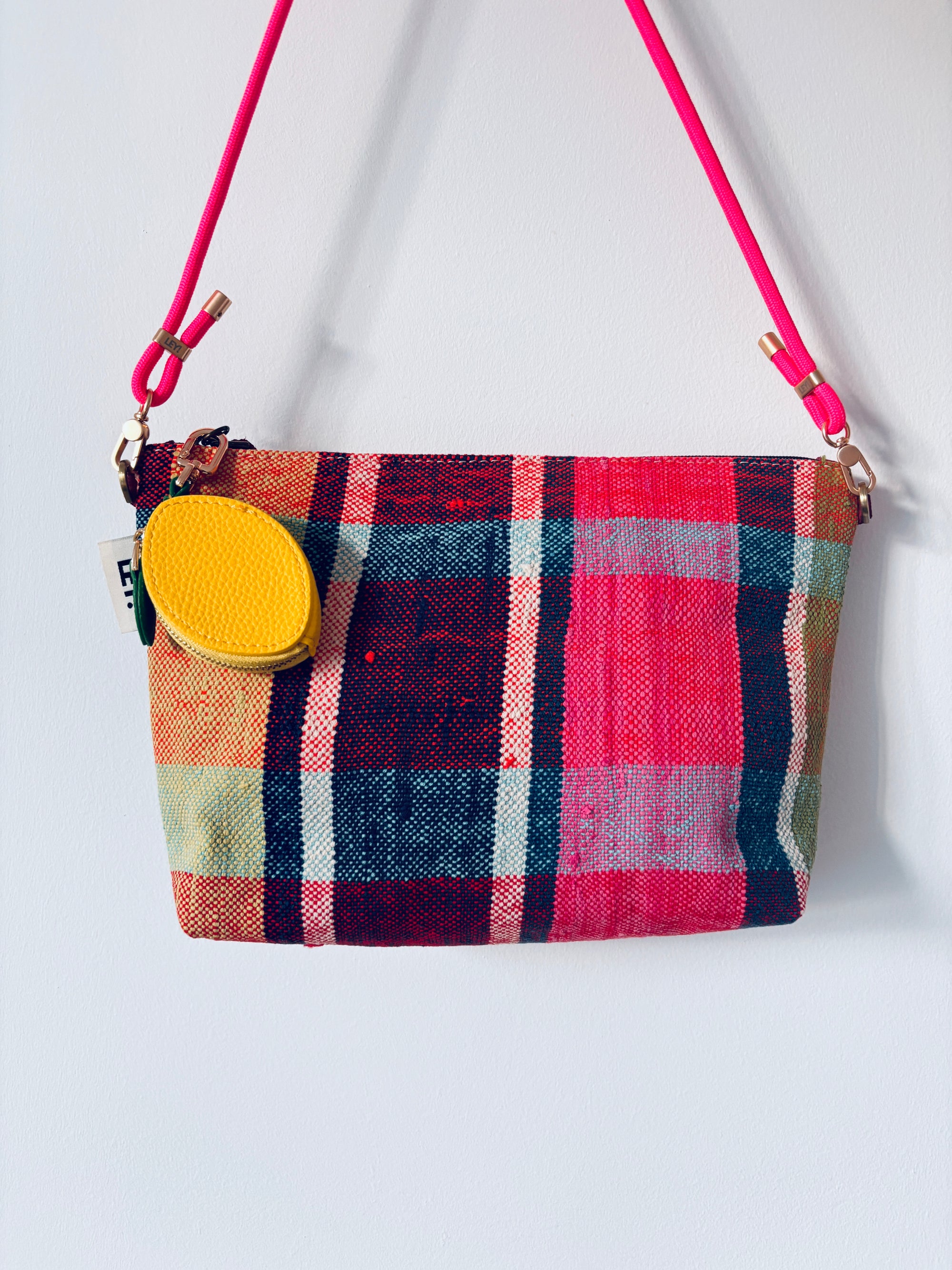 Eine bunt karierte Handtasche mit glattem Reißverschluss bietet der LEY! Schlüsselanhänger - Zitrone und hängt an einem leuchtend pinken Band vor einem schlichten weißen Hintergrund.