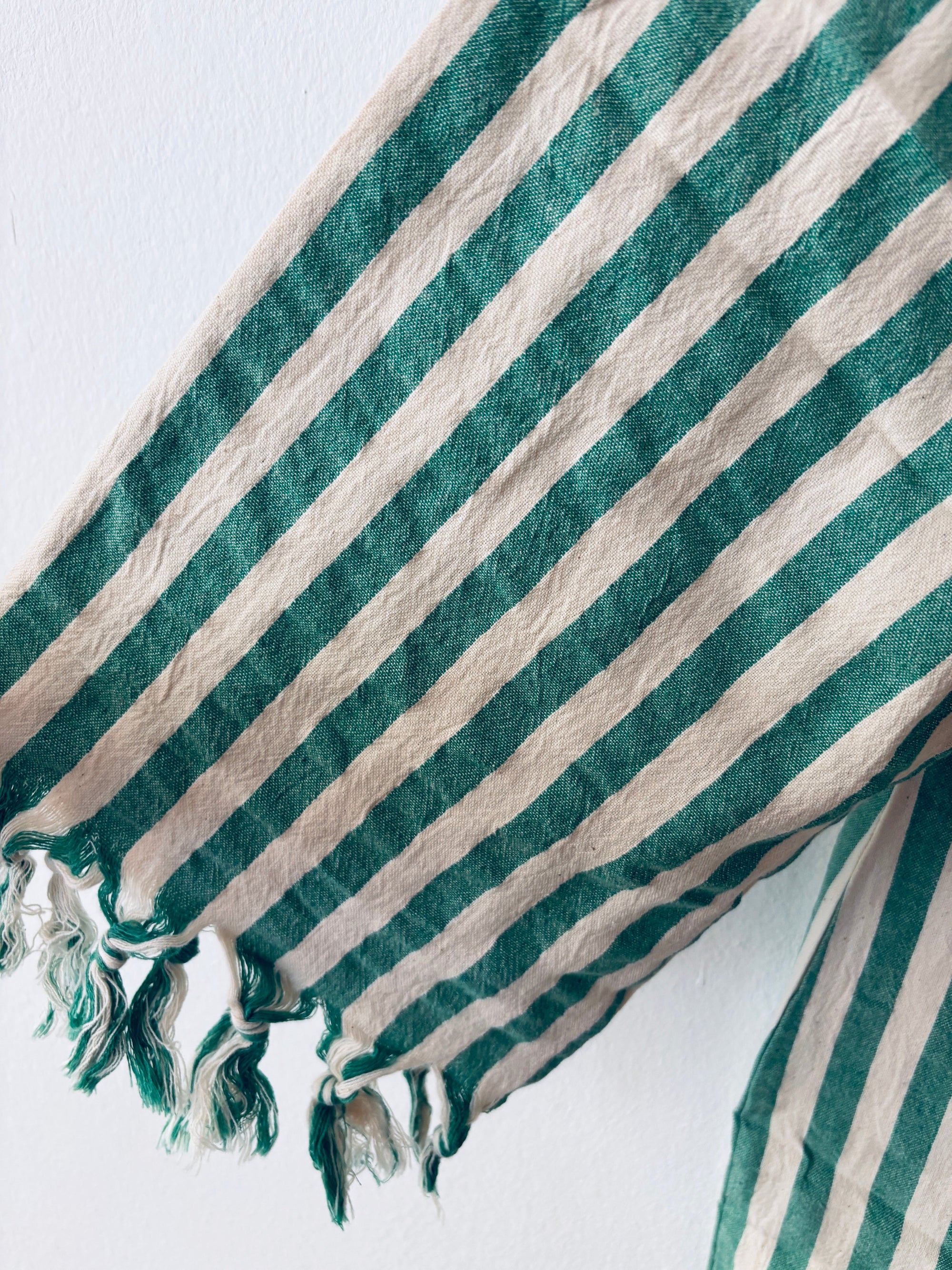 Eine Nahaufnahme des KIMONO - MEDITERANE - GRÜN - WEIß von THE DANISH GIRL INTERIOR zeigt grüne und weiße vertikale Streifen auf einem strukturierten, weichen Stoff mit ausgefransten Kanten und einigen losen Fäden am unteren Rand.
