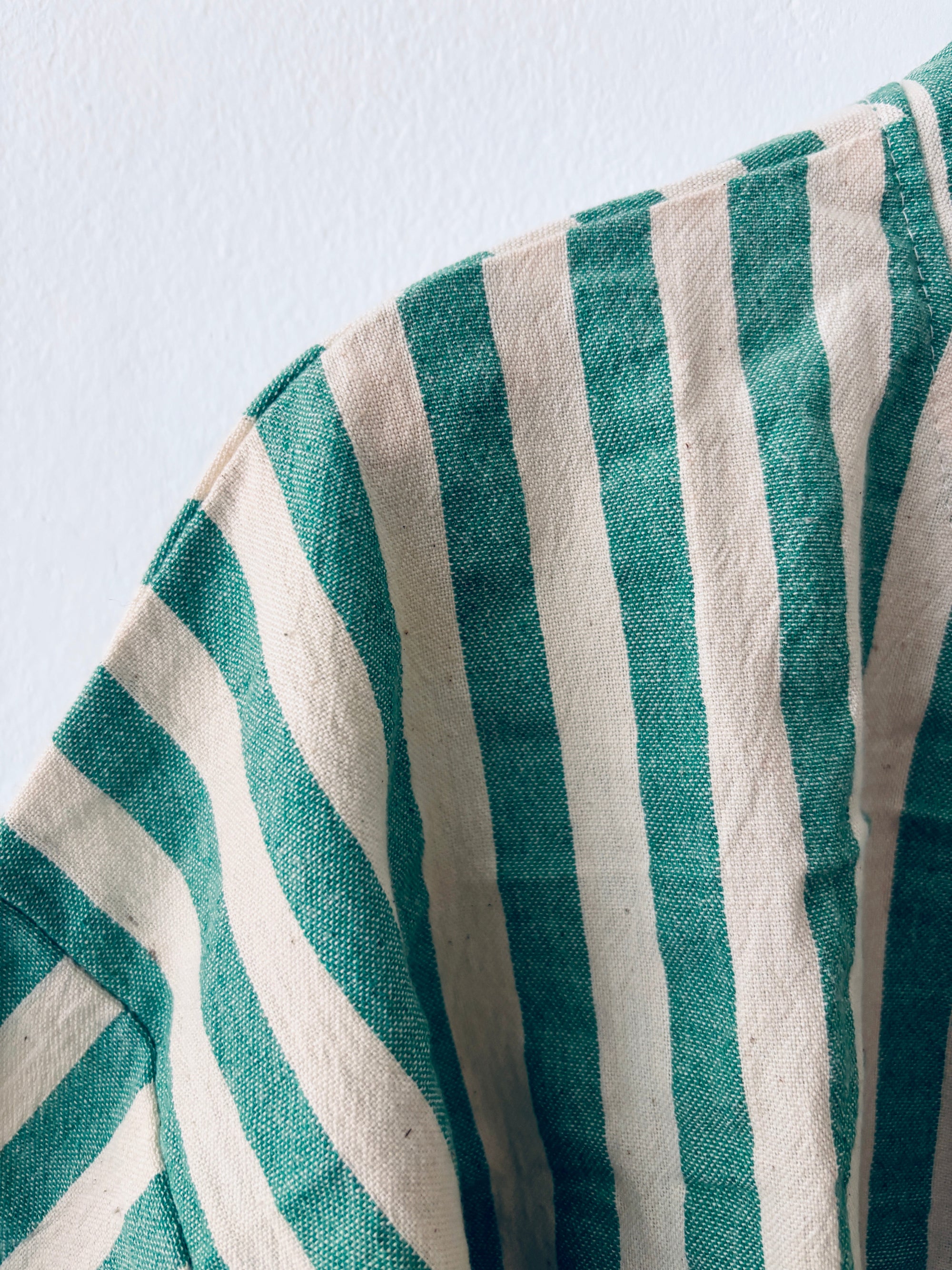 Eine Nahaufnahme des KIMONO - MEDITERANE - GRÜN - WEIß von THE DANISH GIRL INTERIOR zeigt seine vertikalen grünen und weißen Streifen mit sichtbarer Textur und Falten, drapiert vor einem hellen Hintergrund.