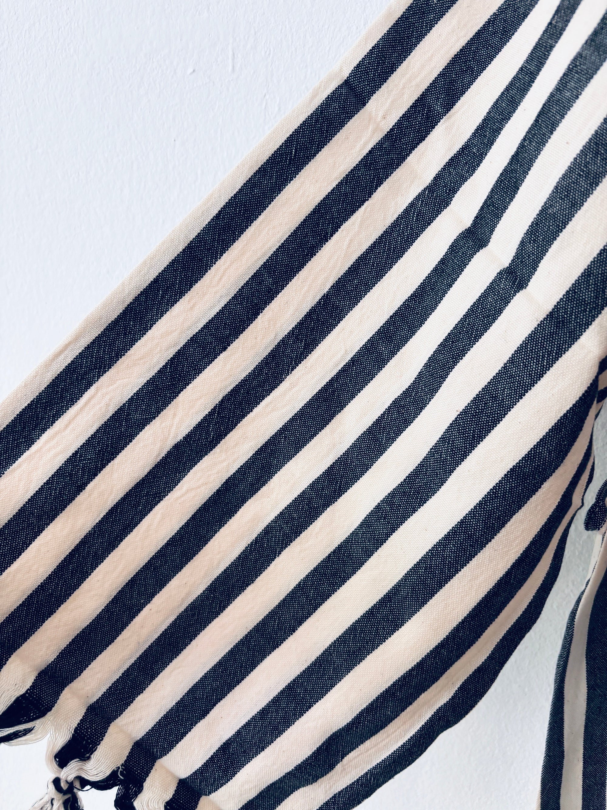 Nahaufnahme des Stoffes KIMONO - MEDITERANE - SCHWARZ - WEIß von THE DANISH GIRL INTERIOR: weich, leicht, mit vertikalen schwarzen und weißen Streifen, an einer Kante leicht gerafft. Perfekt für Mäntel oder Jacken. Abgebildet auf einfarbig weißem Grund.