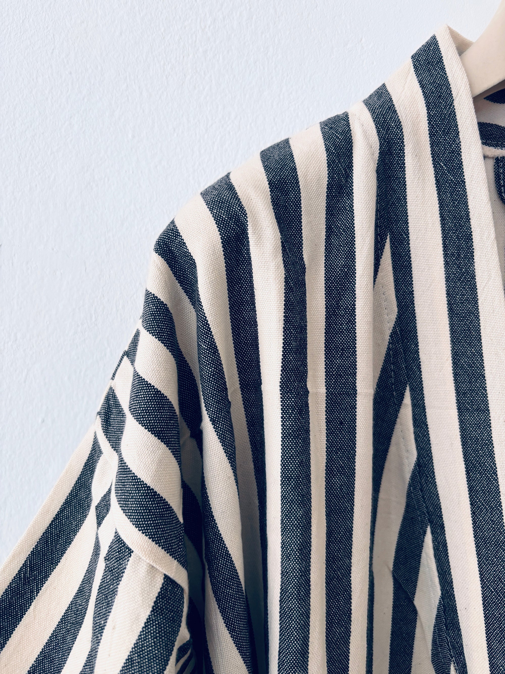 Nahaufnahme des KIMONO - MEDITERANE - SCHWARZ - WEIß von THE DANISH GIRL INTERIOR, mit strukturierten schwarzen und weißen Streifen in vertikalen und diagonalen Mustern auf hellblauem Hintergrund mit Richtungswechsel an den Nähten.