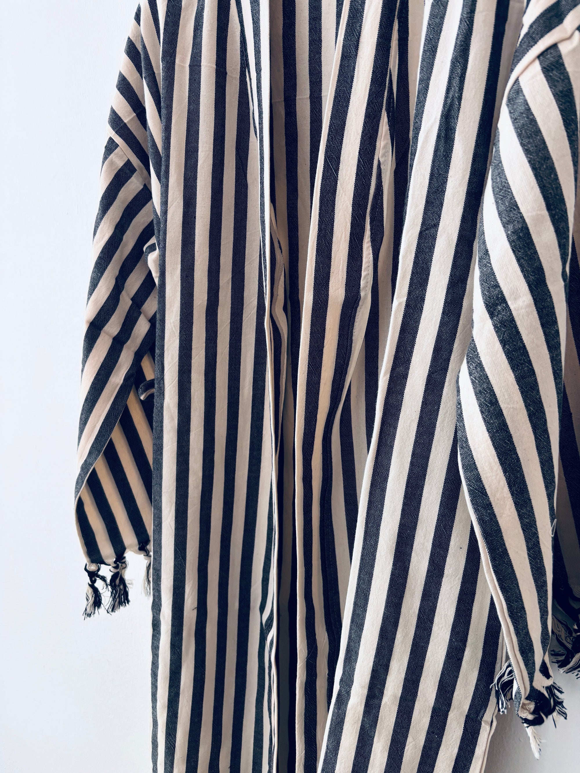 Mehrere KIMONO - MEDITERANE - SCHWARZ - WEIß Roben von THE DANISH GIRL INTERIOR mit schwarz-weißen Streifen und kleinen Quasten hängen aneinander und bilden ein auffälliges, sich wiederholendes Muster vor einem schlichten weißen Hintergrund.