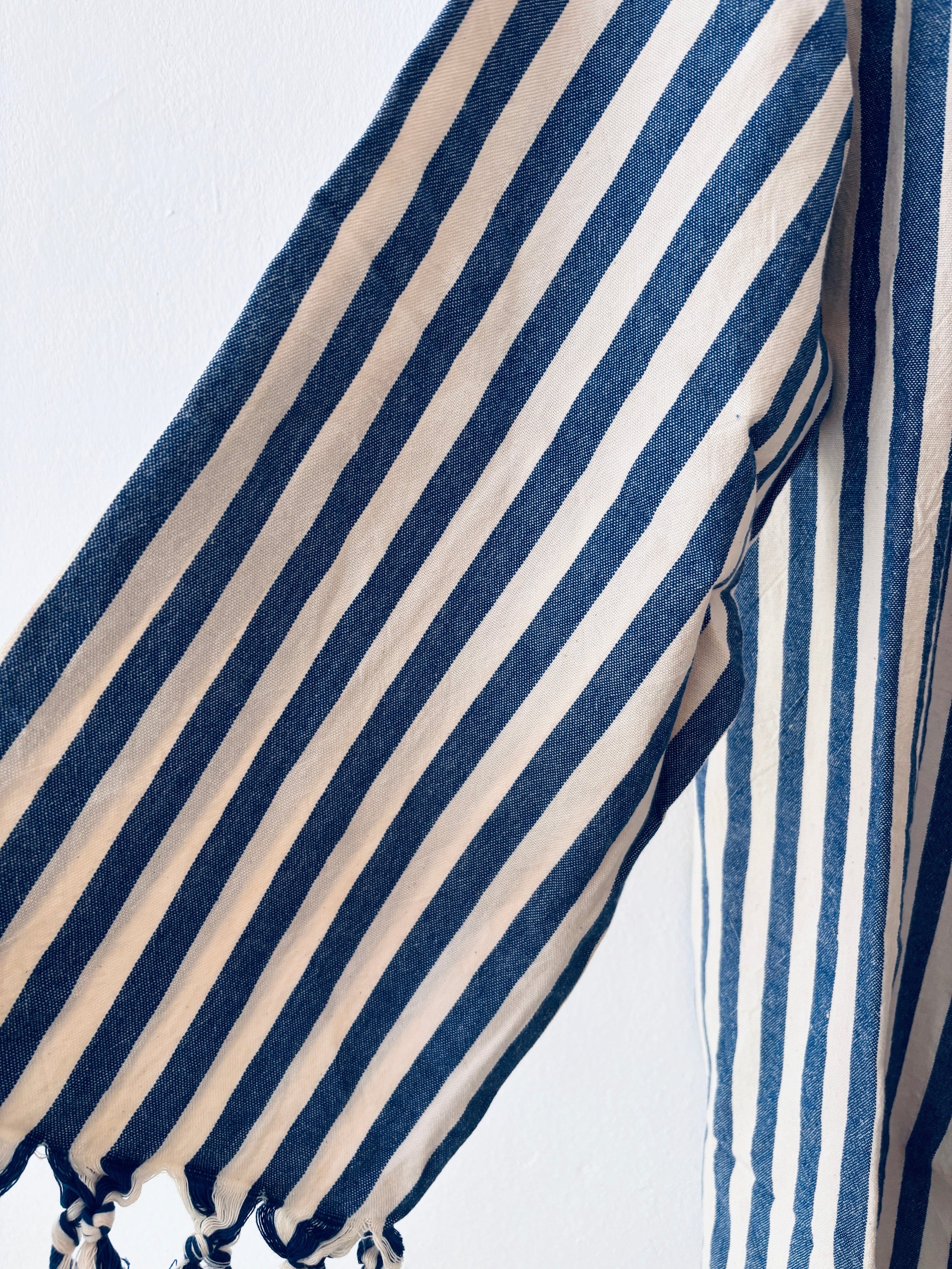 Eine Nahaufnahme des KIMONO - MEDITERANE - BLAU - WEIß von THE DANISH GIRL INTERIOR, mit vertikalen marineblauen und weißen Streifen auf Stoff, drapiert mit einer gerafften Unterkante vor einem schlichten hellen Hintergrund.