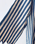 Eine Nahaufnahme des KIMONO - MEDITERANE - BLAU - WEIß von THE DANISH GIRL INTERIOR, mit vertikalen marineblauen und weißen Streifen auf Stoff, drapiert mit einer gerafften Unterkante vor einem schlichten hellen Hintergrund.