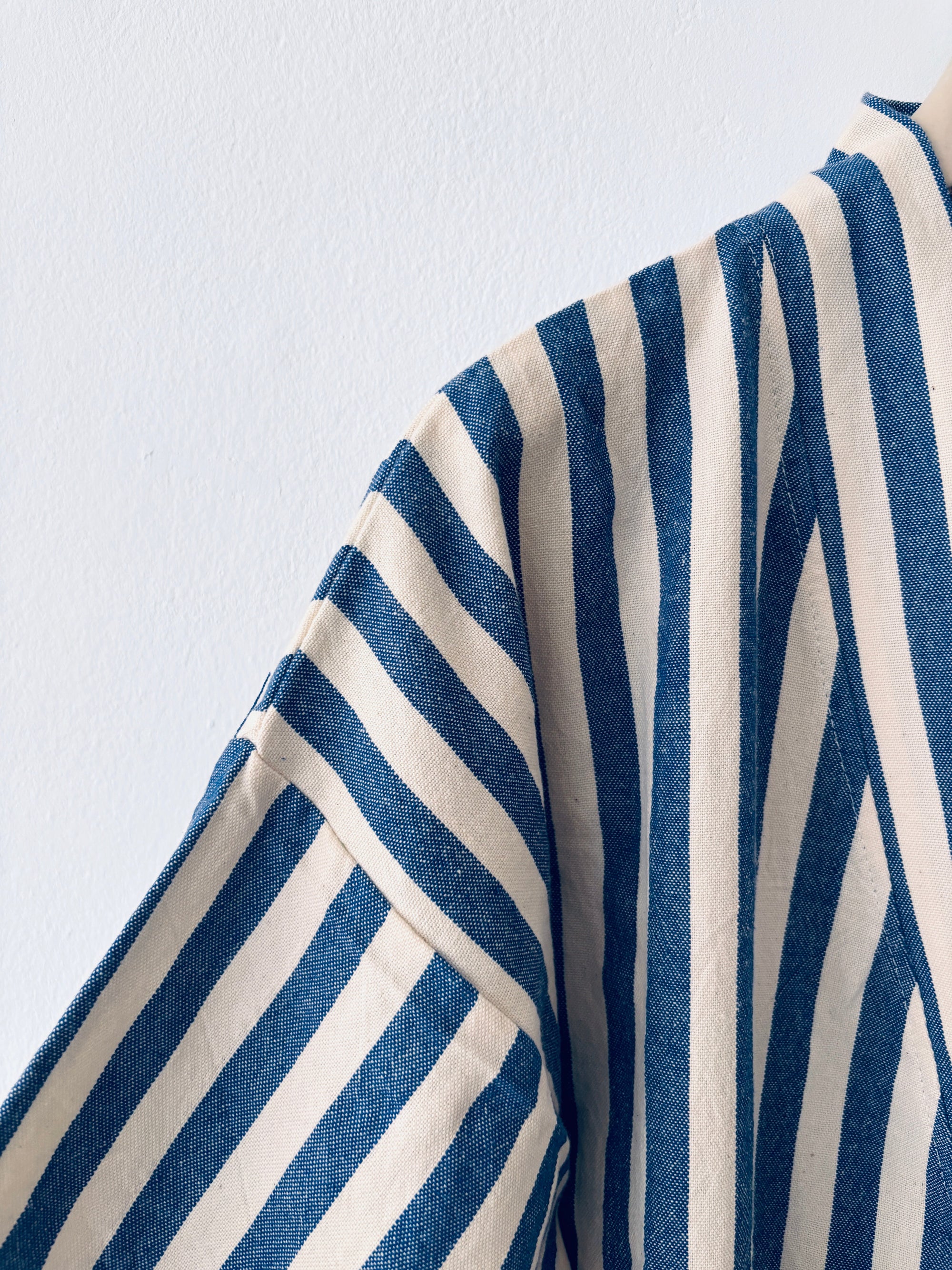 Eine Nahaufnahme des KIMONO - MEDITERANE - BLAU - WEIß von THE DANISH GIRL INTERIOR mit blauen und weißen vertikalen und diagonalen Streifen auf strukturiertem Stoff vor einem schlichten weißen Hintergrund.