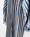 Eine Nahaufnahme des KIMONO - MEDITERANE - BLAU - WEIß von THE DANISH GIRL INTERIOR zeigt die blau-weißen Längsstreifen, lange Ärmel mit ausgefransten Manschetten und einen locker hängenden, leichten Baumwollmantelstoff für einen entspannten Look.