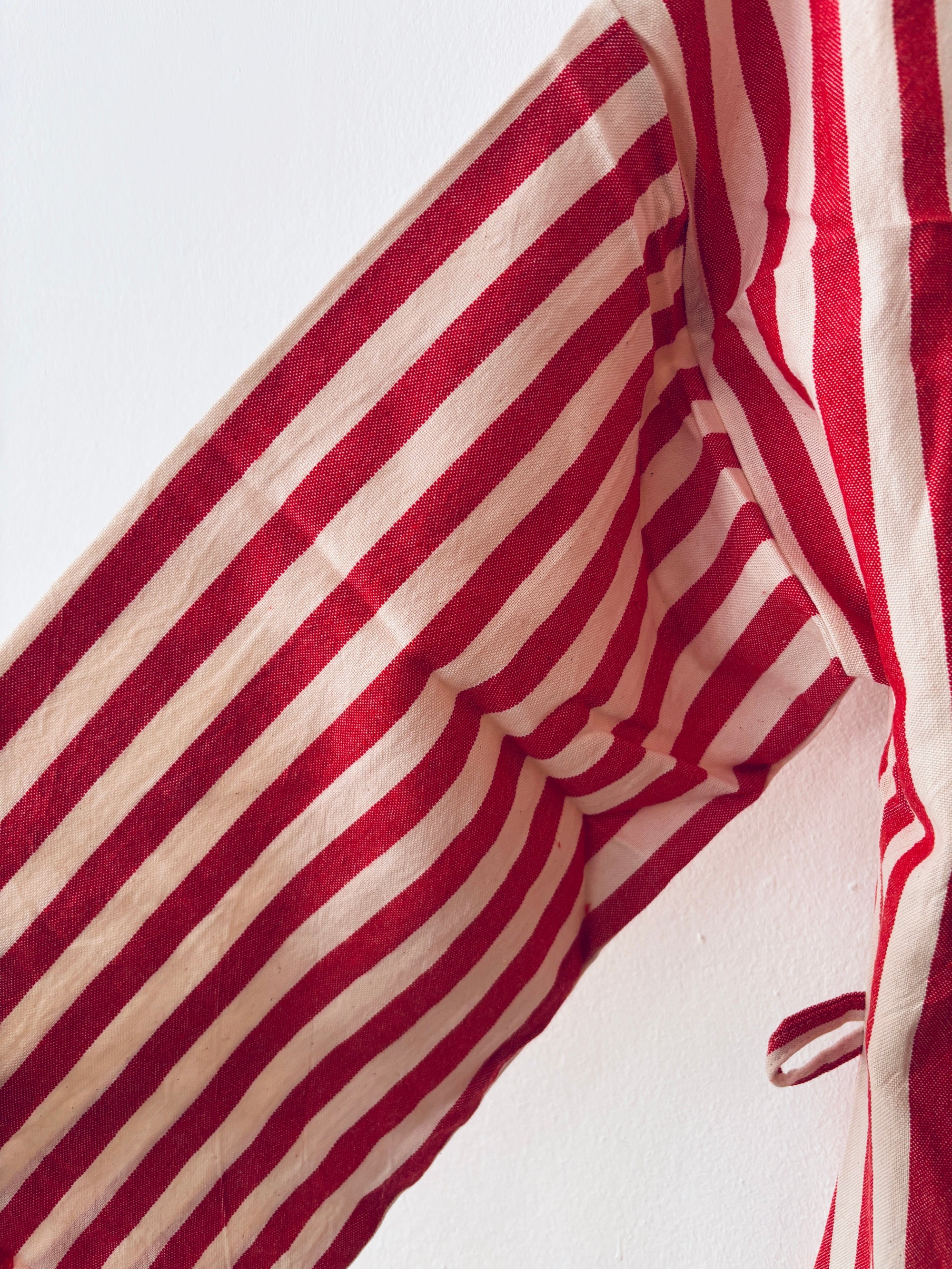 Eine Nahaufnahme des KIMONO - MEDITERANE - ROT - WEIß von THE DANISH GIRL INTERIOR, mit roten und weißen vertikalen Streifen, mit einer detaillierten Ansicht des Ärmels und der Seitennaht vor einem weißen Hintergrund.