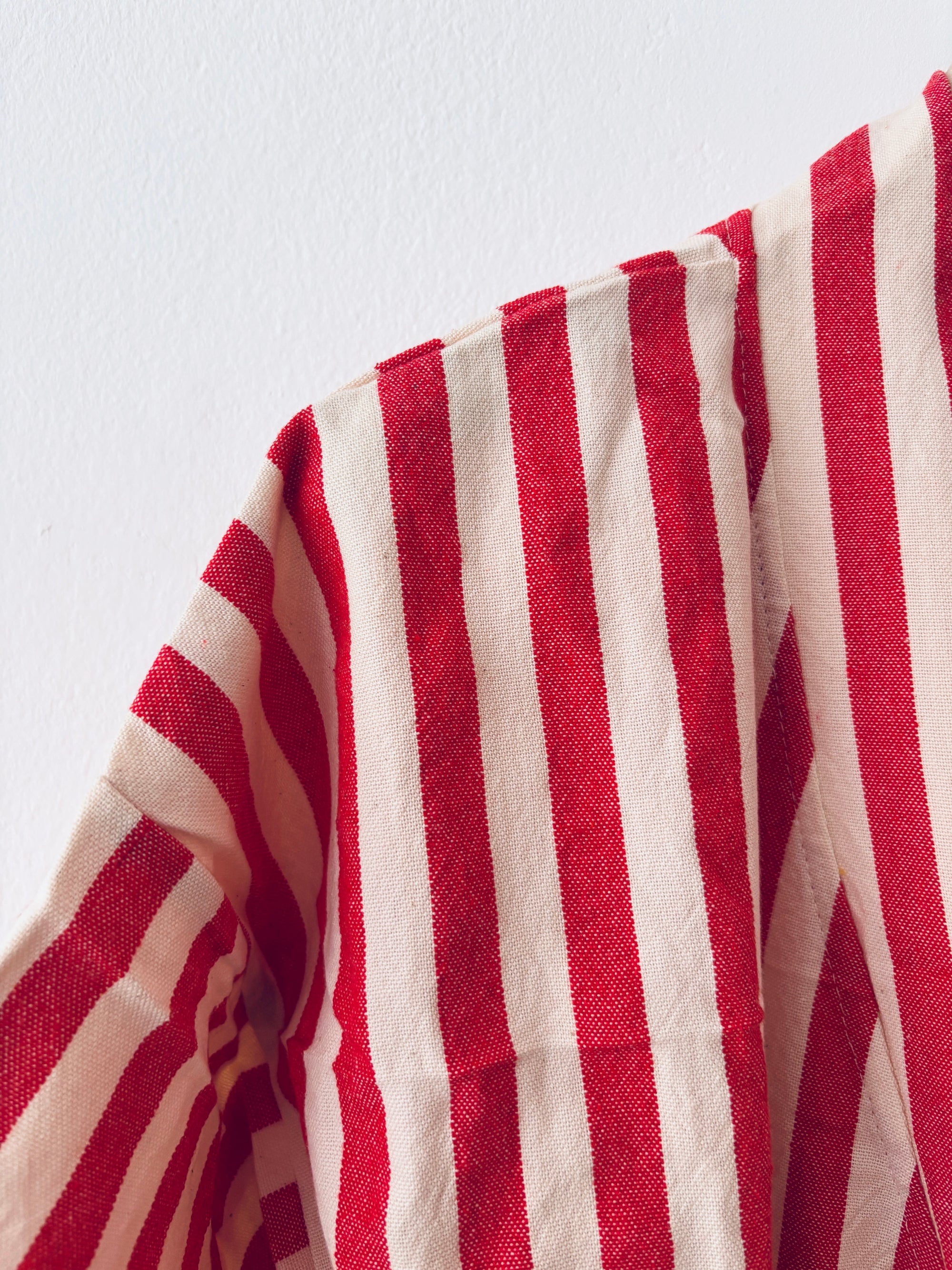 Eine Nahaufnahme des KIMONO - MEDITERANE - ROT - WEIß von THE DANISH GIRL INTERIOR zeigt den rot-weiß gestreiften Stoff, den geschwungenen Saum und einen Teil des Ärmels vor einem schlichten weißen Hintergrund.