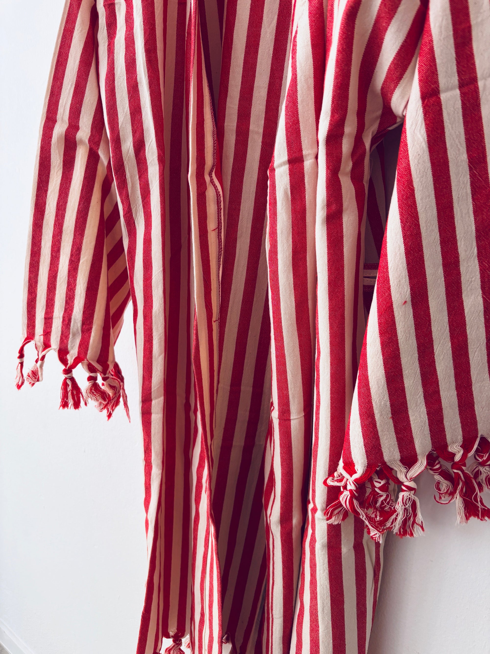 Eine Nahaufnahme des KIMONO - MEDITERANE - ROT - WEIß von THE DANISH GIRL INTERIOR zeigt den rot-weiß gestreiften, strukturierten, leichten Stoff mit ausgefransten Kanten - ideal für einen stilvollen Kimono-Bademantel oder Baumwollmantel.