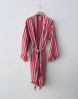 Der KIMONO - MEDITERANE - ROT - WEIß von THE DANISH GIRL INTERIOR mit Gürtel und Quasten hängt an einem Holzkleiderbügel vor einer weißen Wand.