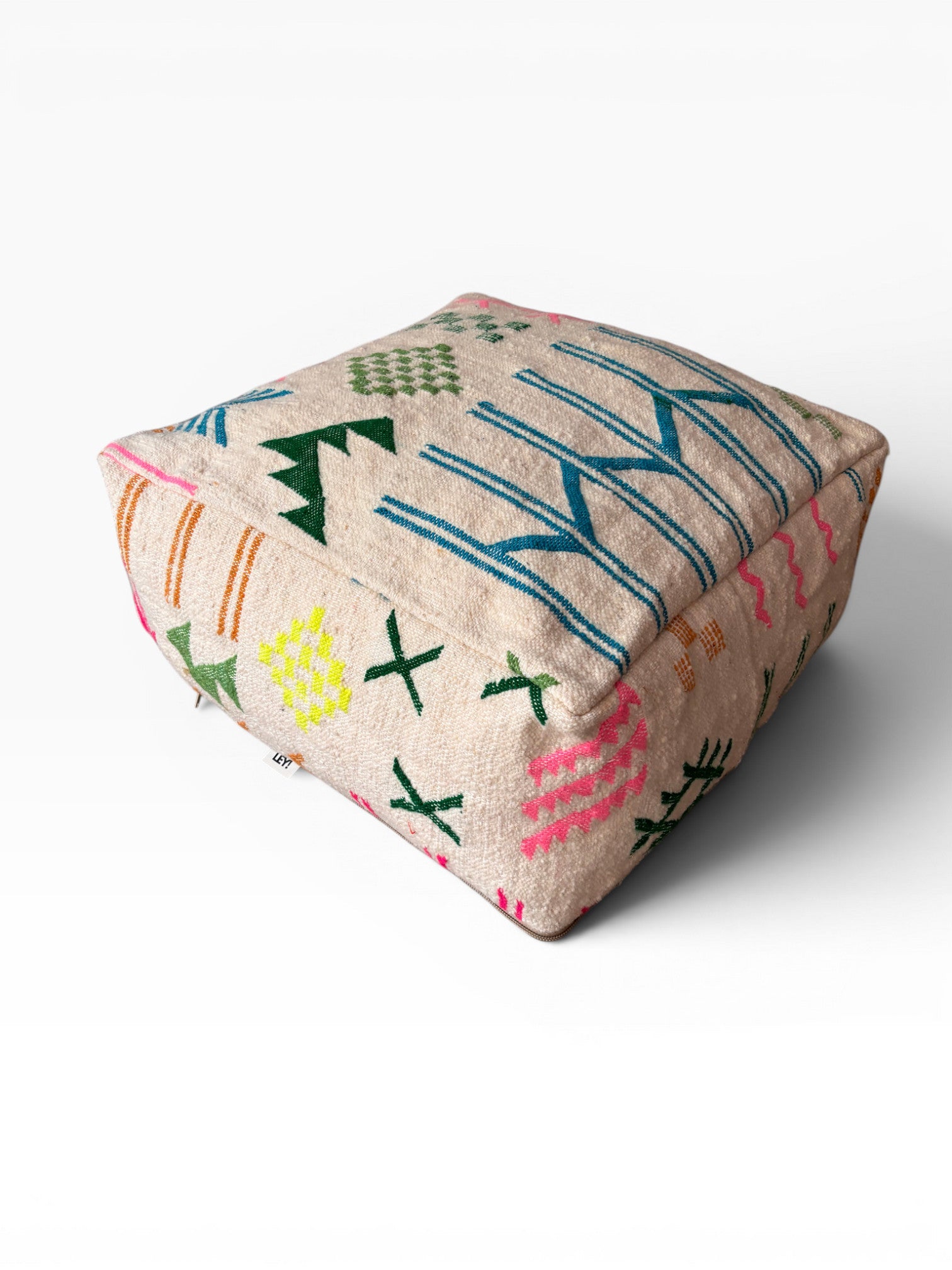 Das Bodenkissen - Colorful Line - Mara von LEY! ist ein quadratischer, beiger Berber-Bodenhocker aus Wolle mit bunten geometrischen Stickereien in Grün, Blau, Pink und Orange auf der Oberseite und an den Seiten vor weißem Hintergrund.