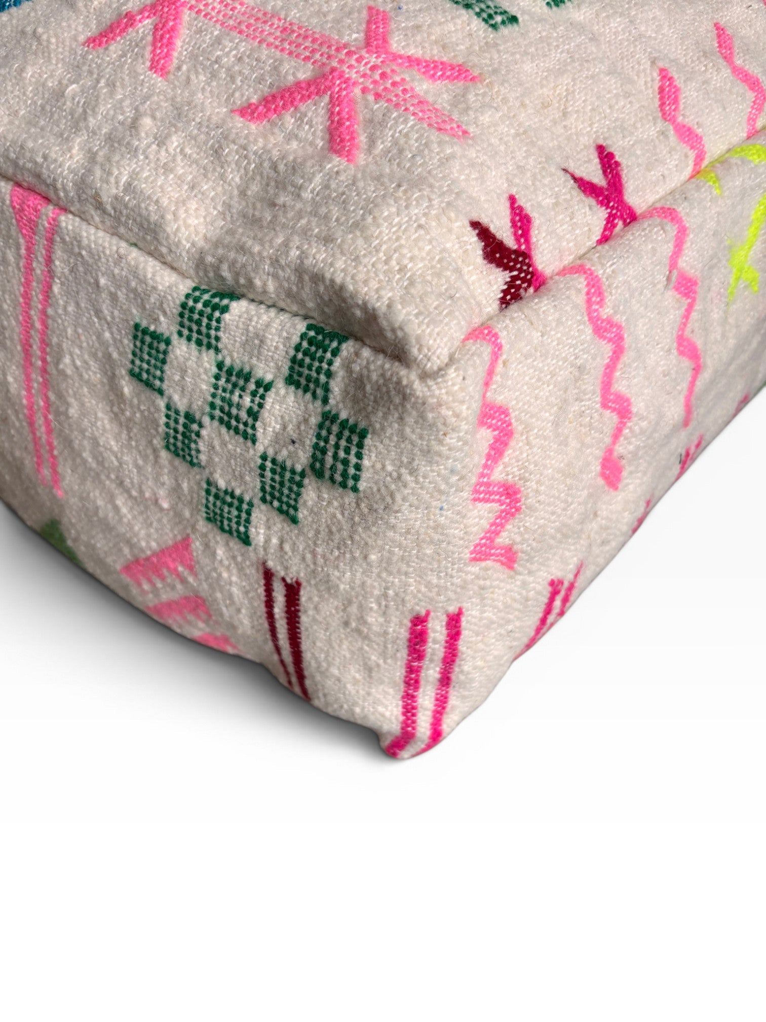 Eine Nahaufnahme der Ecke eines strukturierten, cremefarbenen LEY! Bodenkissen - Colorful Line - Mara aus Wolle mit bunten geometrischen und Zickzack-Stickereien in Rosa, Grün und Rot.