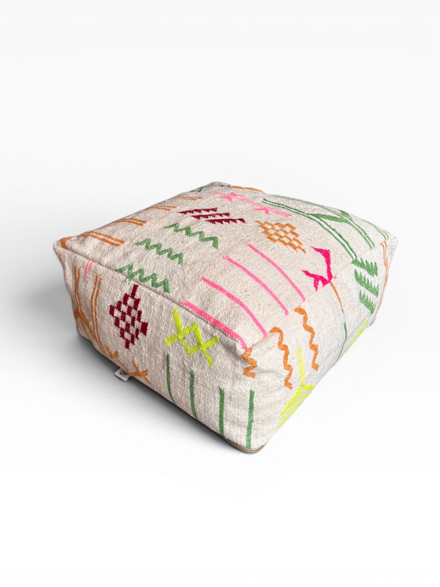 Das LEY! Bodenkissen - Colorful Line - Olea ist ein quadratisches, beiges Boho-Bodenkissen mit leuchtend roten, orangefarbenen, grünen, gelben und rosafarbenen geometrischen und Zickzack-Mustern auf einem einfarbig weißen Hintergrund.