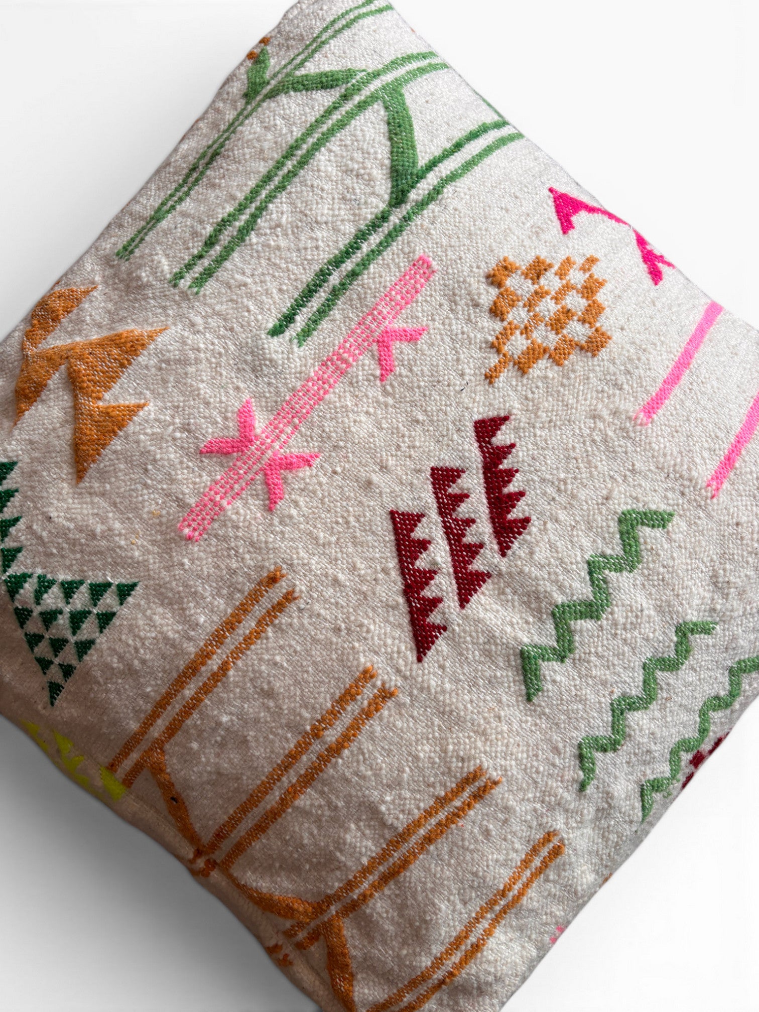Das Bodenkissen - Colorful Line - Olea von LEY! ist ein quadratisches beigefarbenes Wollekissen mit leuchtend grünen, rosa, orangen und roten Stickmustern - ideal als Berber- oder Boho-Sitzkissen auf weißem Hintergrund.