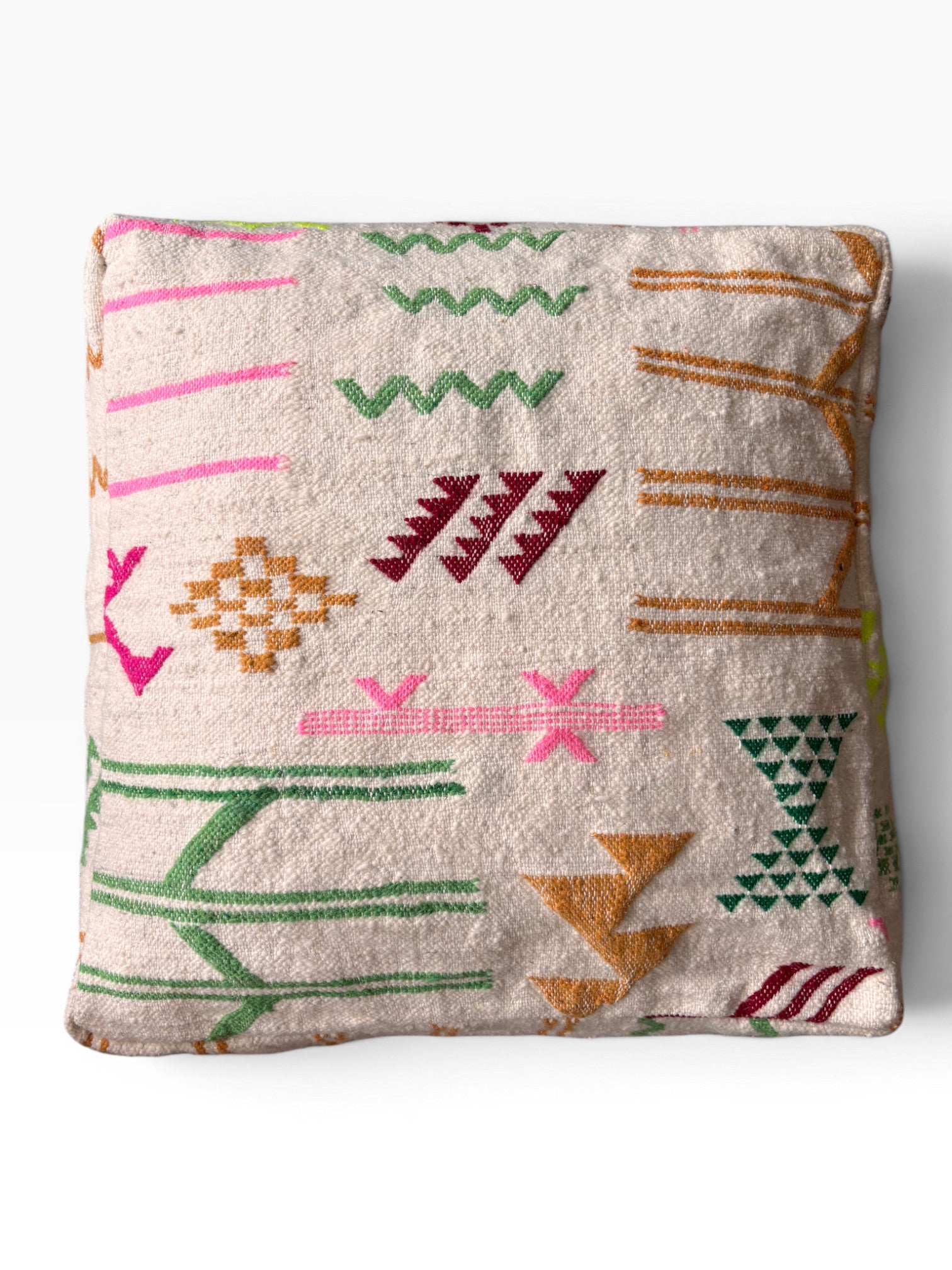 Das LEY! Bodenkissen - Colorful Line - Olea ist ein quadratisches Kissen mit beigefarbenem Hintergrund und leuchtend grünen, rosa, goldenen, orangefarbenen und roten geometrischen Mustern, inspiriert von Berbermustern und hergestellt aus weicher Wolle für gemütlichen Komfort.
