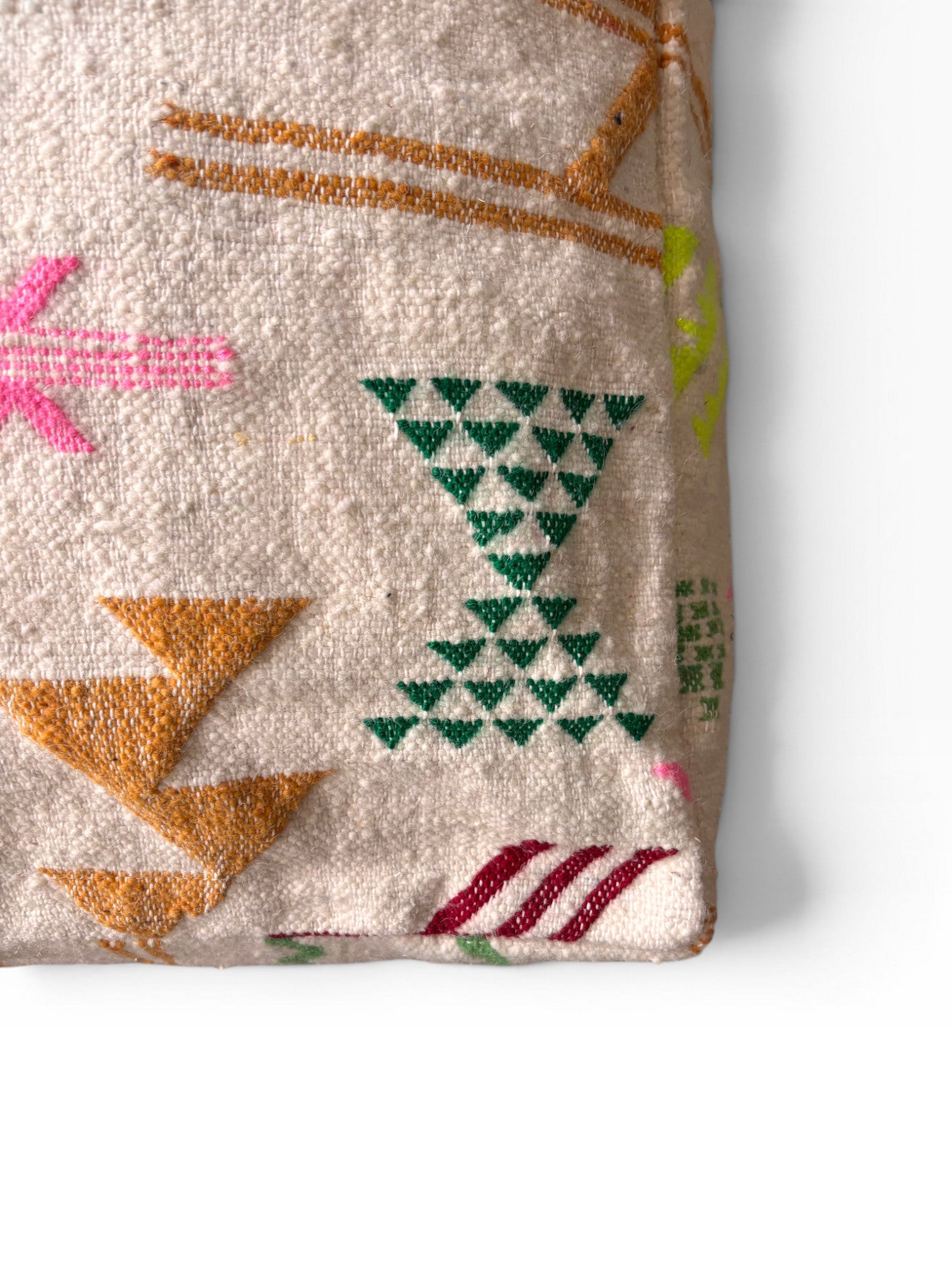Nahaufnahme des LEY! Bodenkissen - Colorful Line - Olea, ein strukturiertes Kissen mit geometrischen Mustern in Grün, Gold, Rosa und Rot auf hellem Beige. Dieses Kissen im Boho-Stil ist teilweise auf einer weißen Oberfläche sichtbar.