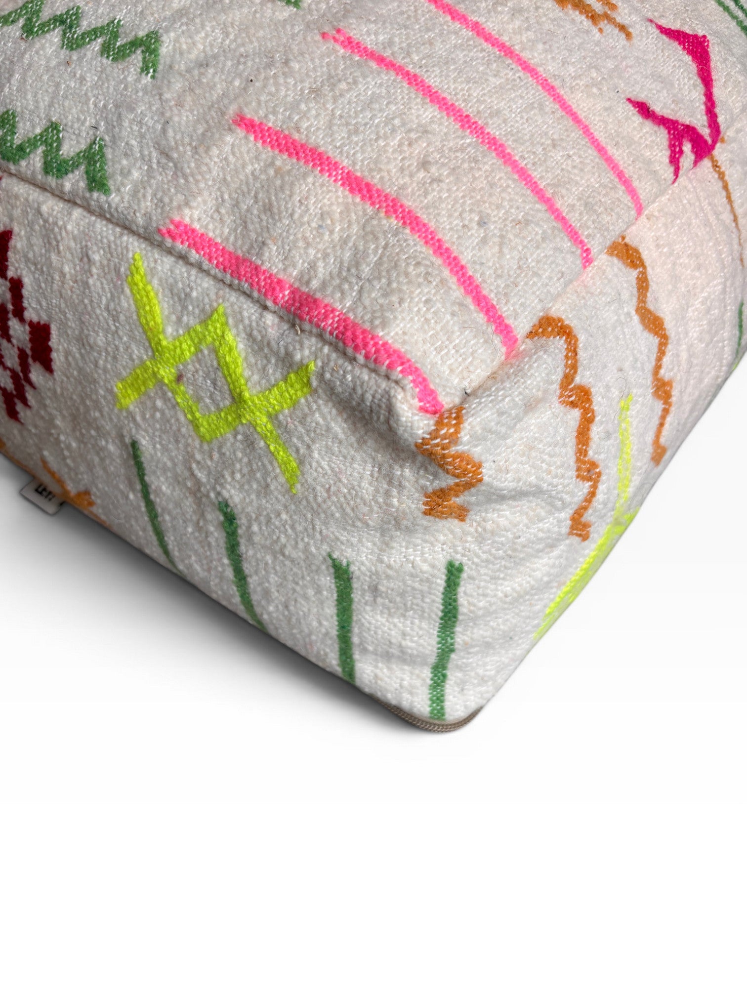 Eine Nahaufnahme des LEY! Bodenkissen - Colorful Line - Olea, einem weißen, strukturierten Bodenkissen mit leuchtend grünen, gelben, rosa und orangefarbenen, abstrakten Stickmustern auf der Oberfläche und den Seiten.