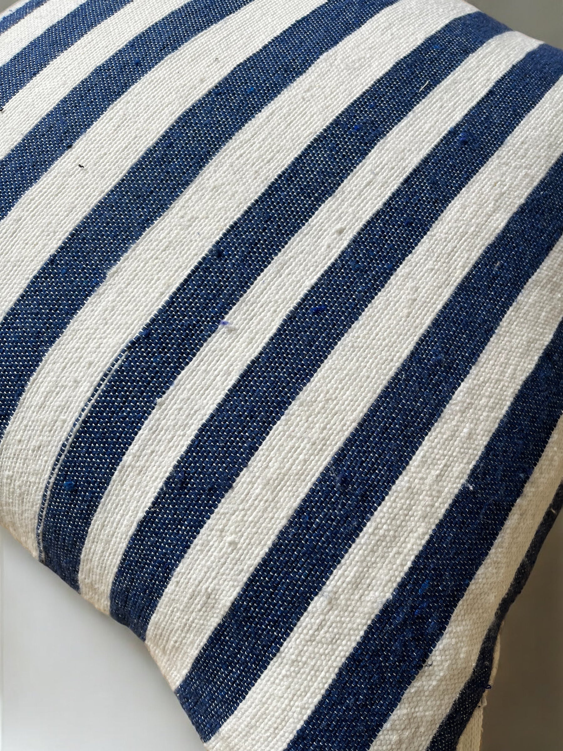 Eine Nahaufnahme eines LEY! Kissen - Hellas 60x60 mit strukturiertem Stoff, der abwechselnd marineblaue und cremefarbene Längsstreifen aufweist.