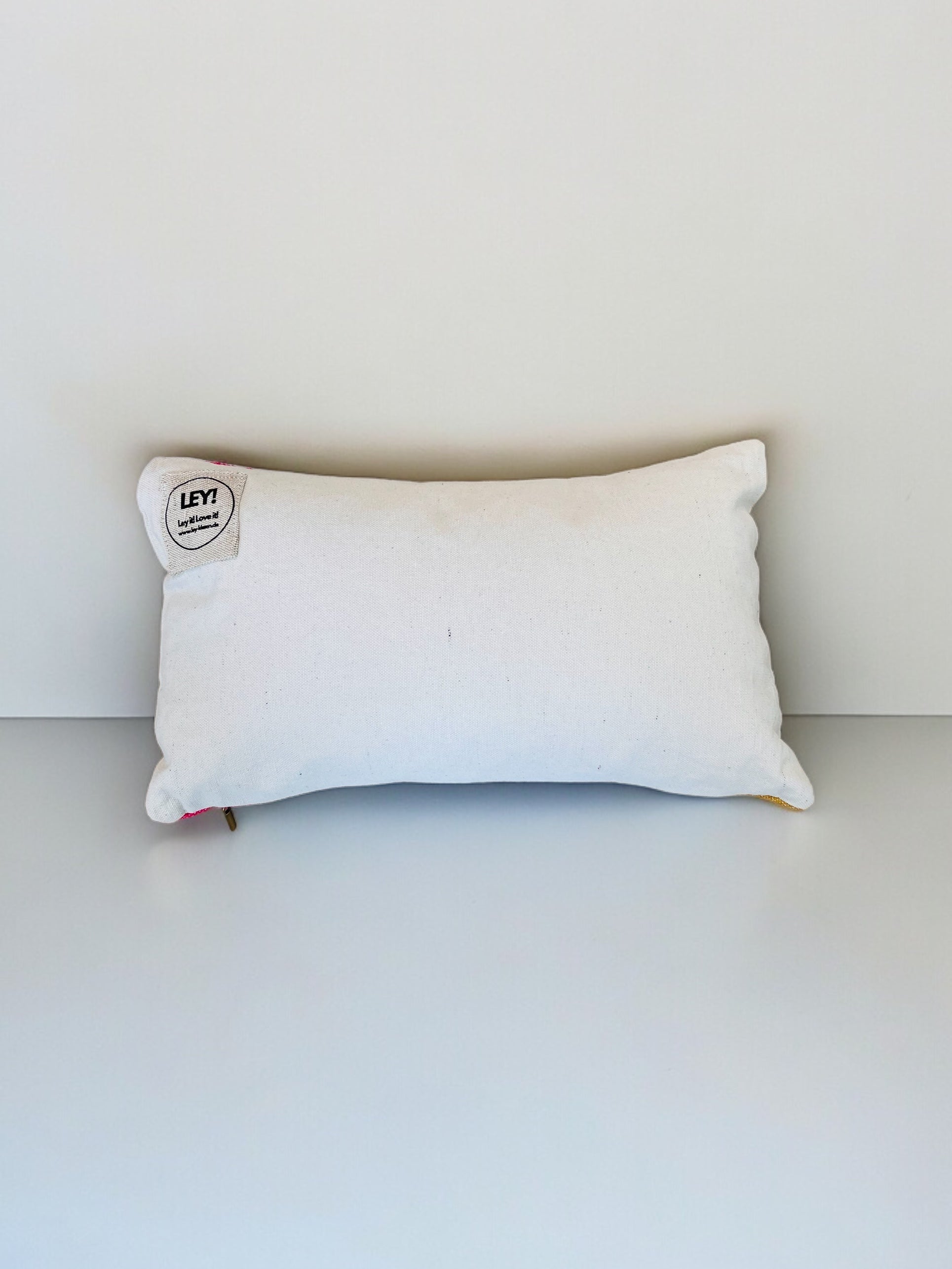 Ein rechteckiges weißes Kissen - Asma 30x50 von LEY! mit einem kleinen runden LEY!-Aufnäher in der linken oberen Ecke, vor einem schlichten weißen Hintergrund.
