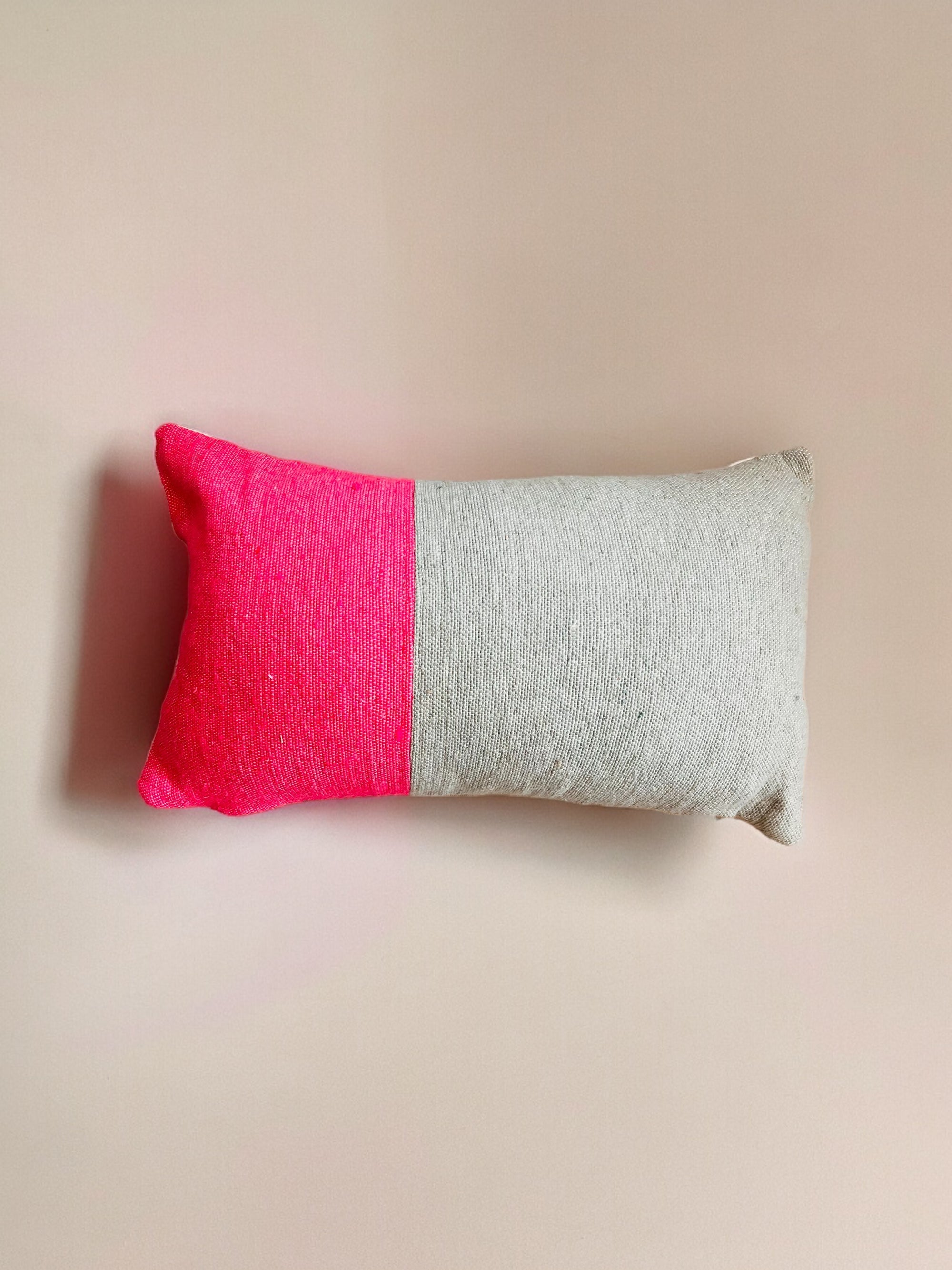 Das Kissen - Merva 30x50 von LEY! ist handgefertigt aus Baumwolle, inspiriert von Marrakesch: rechteckig mit zwei Farbblöcken - leuchtendes Pink links, helles Grau rechts - auf beigem Grund.
