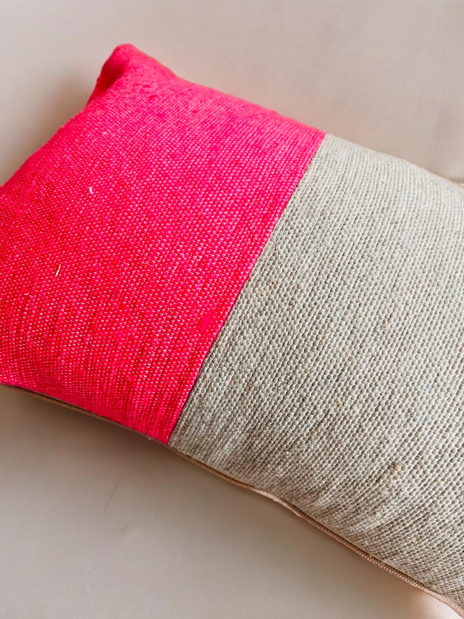 Das Kissen - Merva 30x50 von LEY! ist ein rechteckiges, handgefertigtes Kissen mit einem strukturierten Bezug in leuchtendem Pink und Beige aus der Spring Line, dargestellt auf einer neutralen Oberfläche.