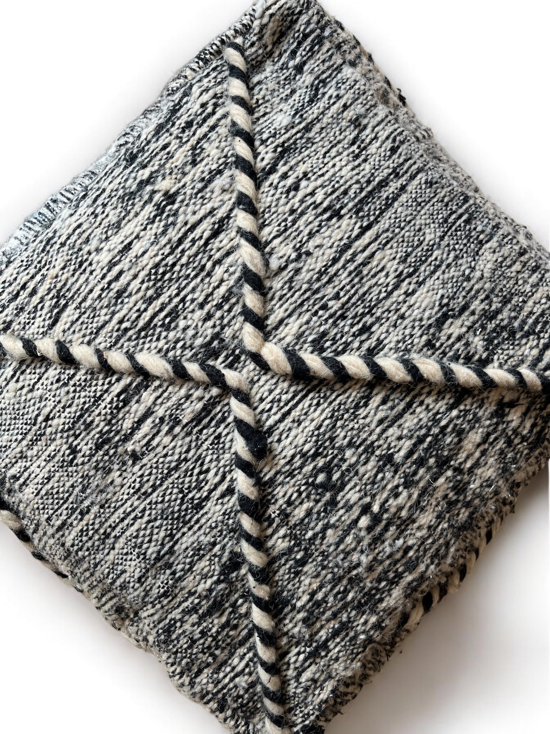 Das Kleines Bodenkissen - Mica Mini von LEY! ist ein handgefertigtes, quadratisches Kissen aus hochwertiger Schurwolle. Es hat ein schwarz-weiß marmoriertes Muster, vier Abschnitte, die durch gedrehte Kordeln unterteilt sind, und einen schlichten weißen Hintergrund.