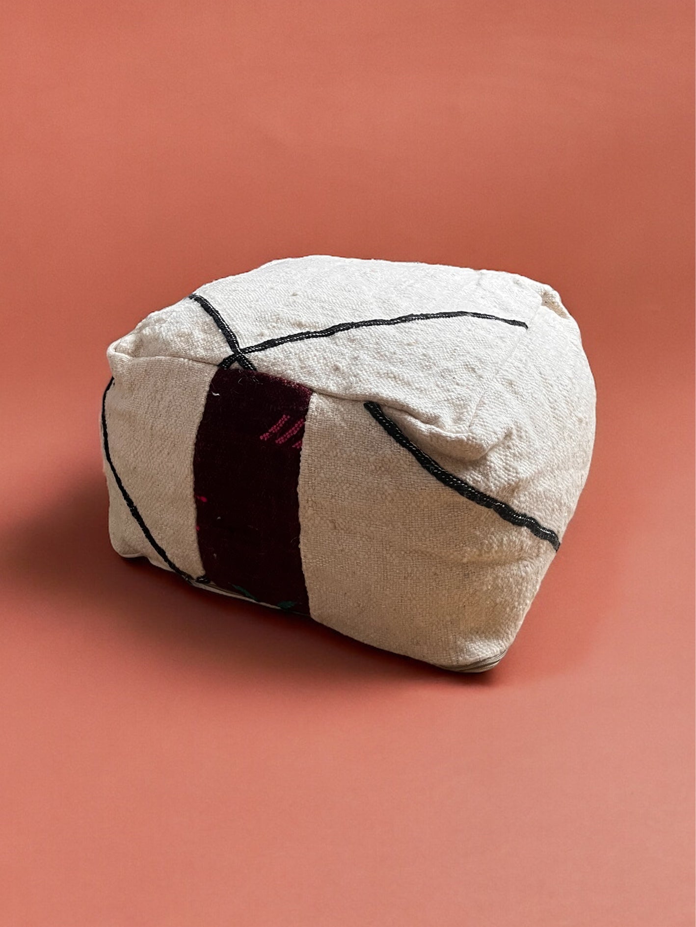 Das Kleine Bodenkissen - Mera Mini von LEY! besticht durch handgefertigten Charme mit cremefarbener Schurwolle, schwarzen Linienmustern, einem dunkelkastanienbraunen Längsstreifen und einem unifarbenen Terrakotta-Fond für einen stilvollen Akzent.