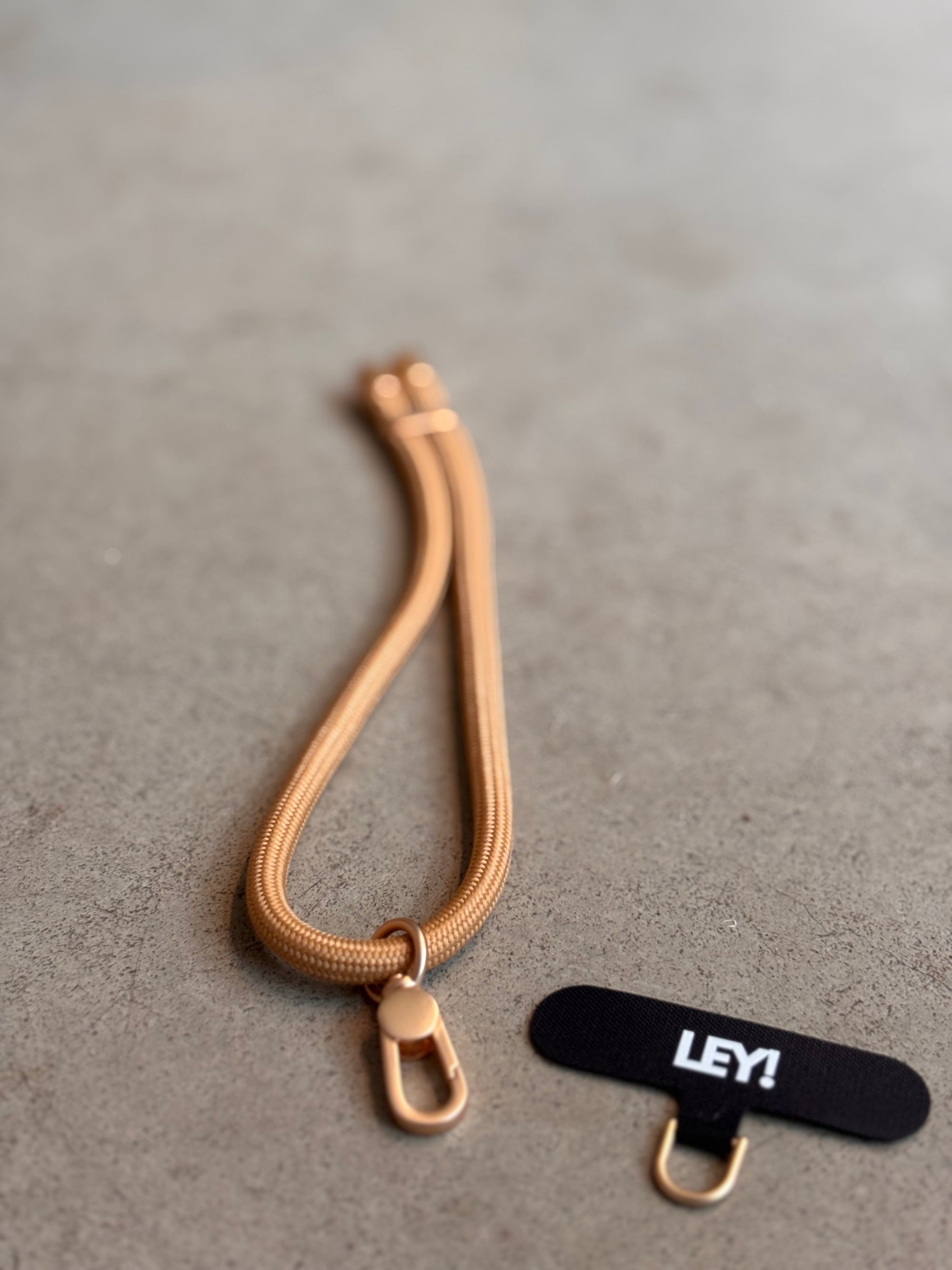 Ein Schlüsselanhänger von LEY! mit runder Schließe und Haken liegt auf einer grauen Fläche neben einem schwarzen Stoffanhänger mit der Aufschrift "LEY!", inspiriert von trendigen Farben und Lanyard Handyband Style.