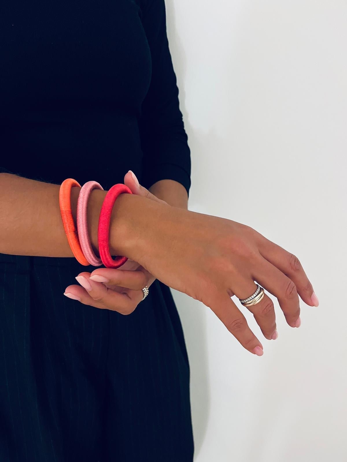 Eine schwarz gekleidete Person trägt am linken Arm vier farbenfrohe, marokkanisch inspirierte Armreifen mit Garnumwicklung, darunter den "Armreif - mint" von LEY! sowie einen silbernen Ring vor einem schlichten weißen Hintergrund.