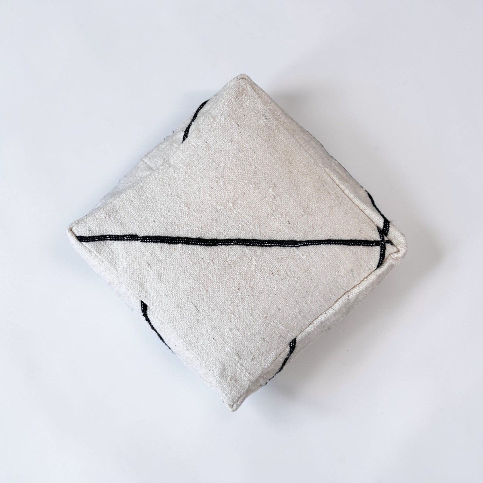 Das Kleine Bodenkissen - Meli Mini von LEY! besteht aus handgefertigter Schurwolle in strukturiertem Off-White, akzentuiert mit einer einfachen schwarzen Linie, auf einem schlichten weißen Hintergrund - ideal als stilvolles Bodenkissen.