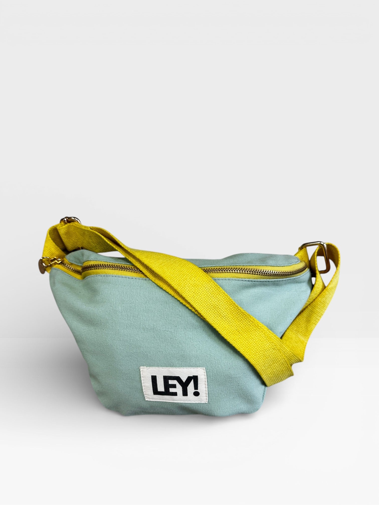 Die LEY! Bauchtasche - MINT-GELB von LEY! ist eine mint-gelbe Crossbody-Tasche mit einem gelben, verstellbaren Riemen, Reißverschluss und einem weißen Aufnäher mit schwarzem "LEY!"-Schriftzug auf der Vorderseite - perfekt als Festival-Gürteltasche.