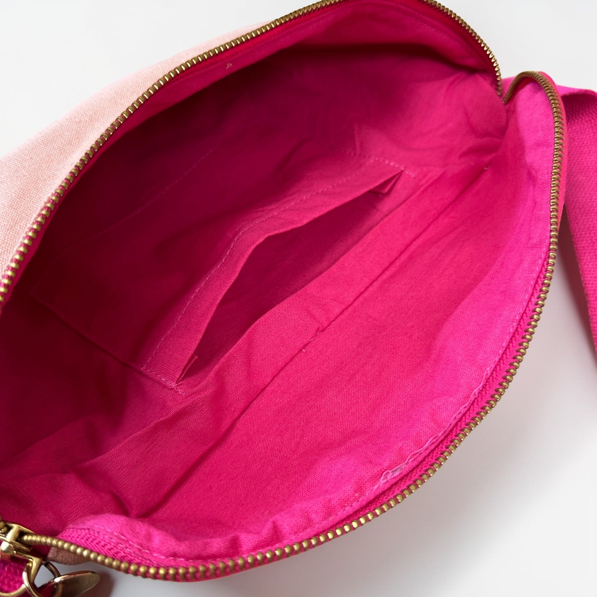 Die LEY! Bauchtasche - NUDE-PINK ist eine offene, pinkfarbene Gürteltasche aus Stoff mit einem goldenen Reißverschluss, einem hellrosa Futter und einer Innentasche. Leer und flach dargestellt, betont sie ihr geräumiges Inneres - ideal für Ihr nächstes Festival. Marke: LEY!.