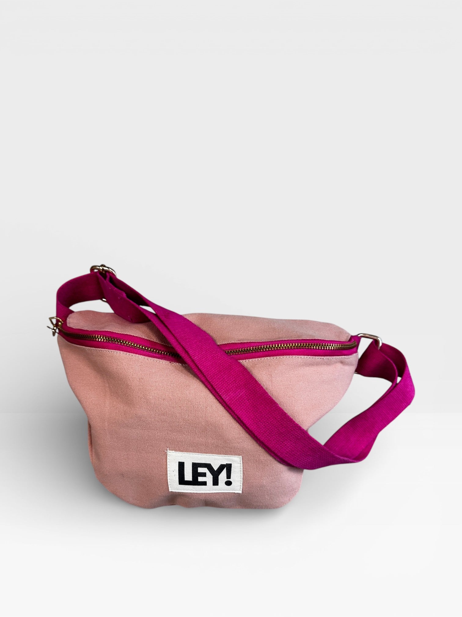 Die LEY! Bauchtasche - NUDE-PINK ist eine hellrosa Crossbody-Tasche mit einem hellrosa Riemen, Reißverschluss und einem weißen "LEY!"-Aufnäher auf der Vorderseite - perfekt für jedes Festival.