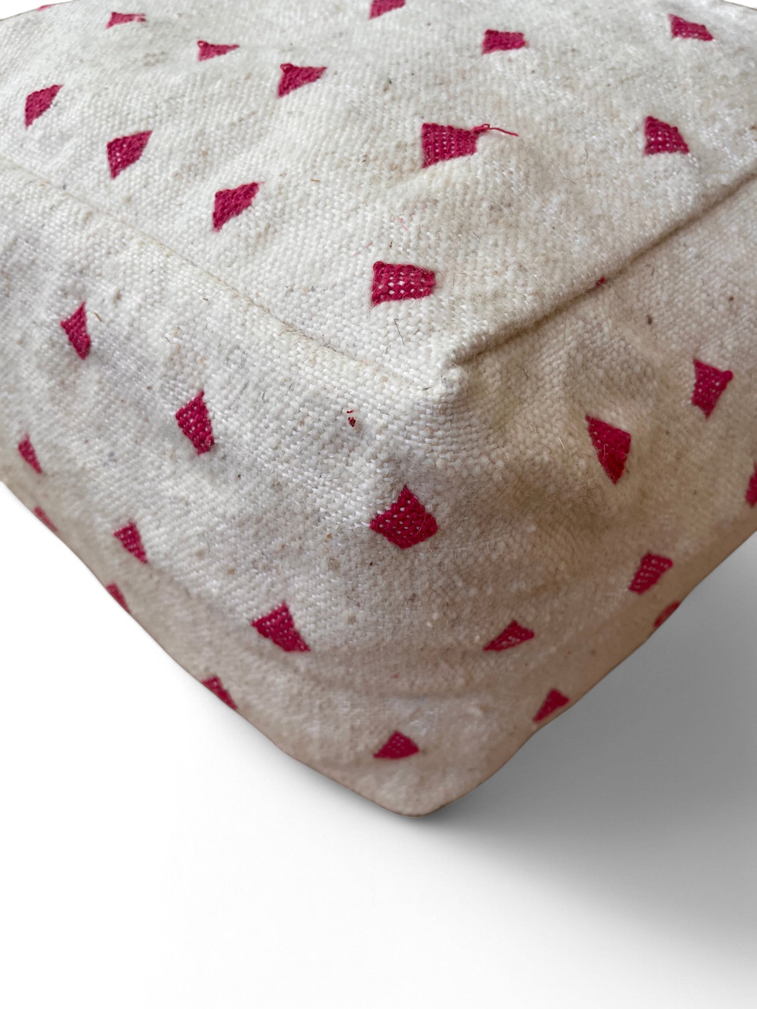 Eine Nahaufnahme des LEY! Kleines Bodenkissen - Mona Mini Lila mit kleinen roten Dreiecken auf beiger Schurwolle hebt die detailreiche Handarbeit aus Marrakesch vor einem weißen Hintergrund hervor.