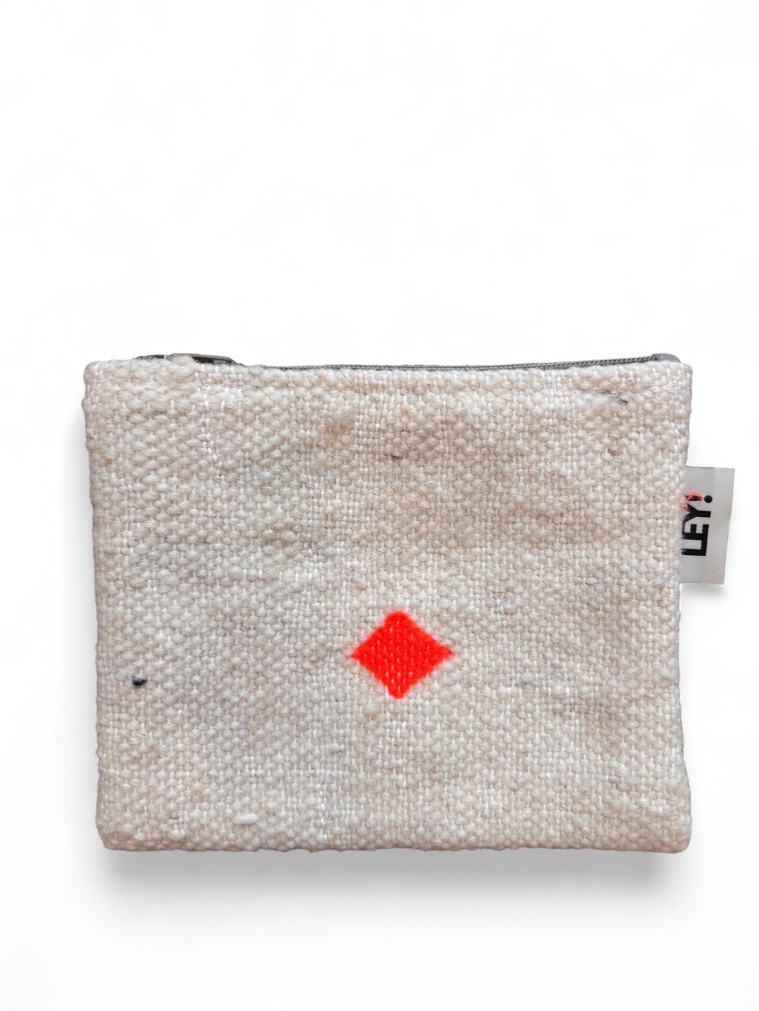 Die LEY! Tasche - Colorful Line (15x20cm) ist eine kleine, quadratische, beigefarbene Tasche aus Schurwolle Handarbeit, mit strukturierter Oberfläche, Reißverschluss oben, leuchtend rotem Rautenmuster in der Mitte und einem seitlichen Anhänger im Stil von Marrakesch Accessoire.