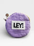 Der LEY! Coinholder - FLIEDER-GELB von LEY! ist ein runder lilafarbener Stoffbeutel mit Metallreißverschluss, kleinem Anhänger und weißem Aufnäher mit schwarzem "LEY!"-Schriftzug auf der Vorderseite - ideal als Schlüsselanhänger oder stylischer Münzhalter.