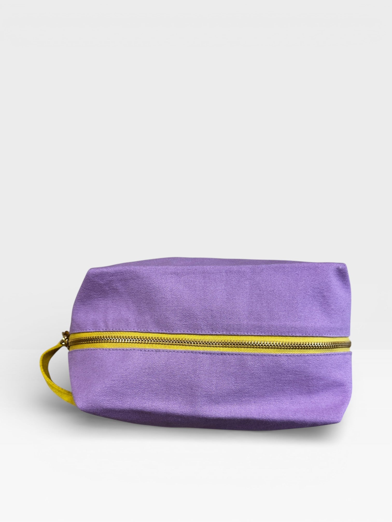 Der LEY! Pouch - FLIEDER-GELB von LEY! ist ein rechteckiger lavendelfarbener Beutel mit gelbem Reißverschluss und Handschlaufe, ideal für Kulturbeutel Reisen, abgebildet auf einer weißen Fläche mit hellgrauem Hintergrund.