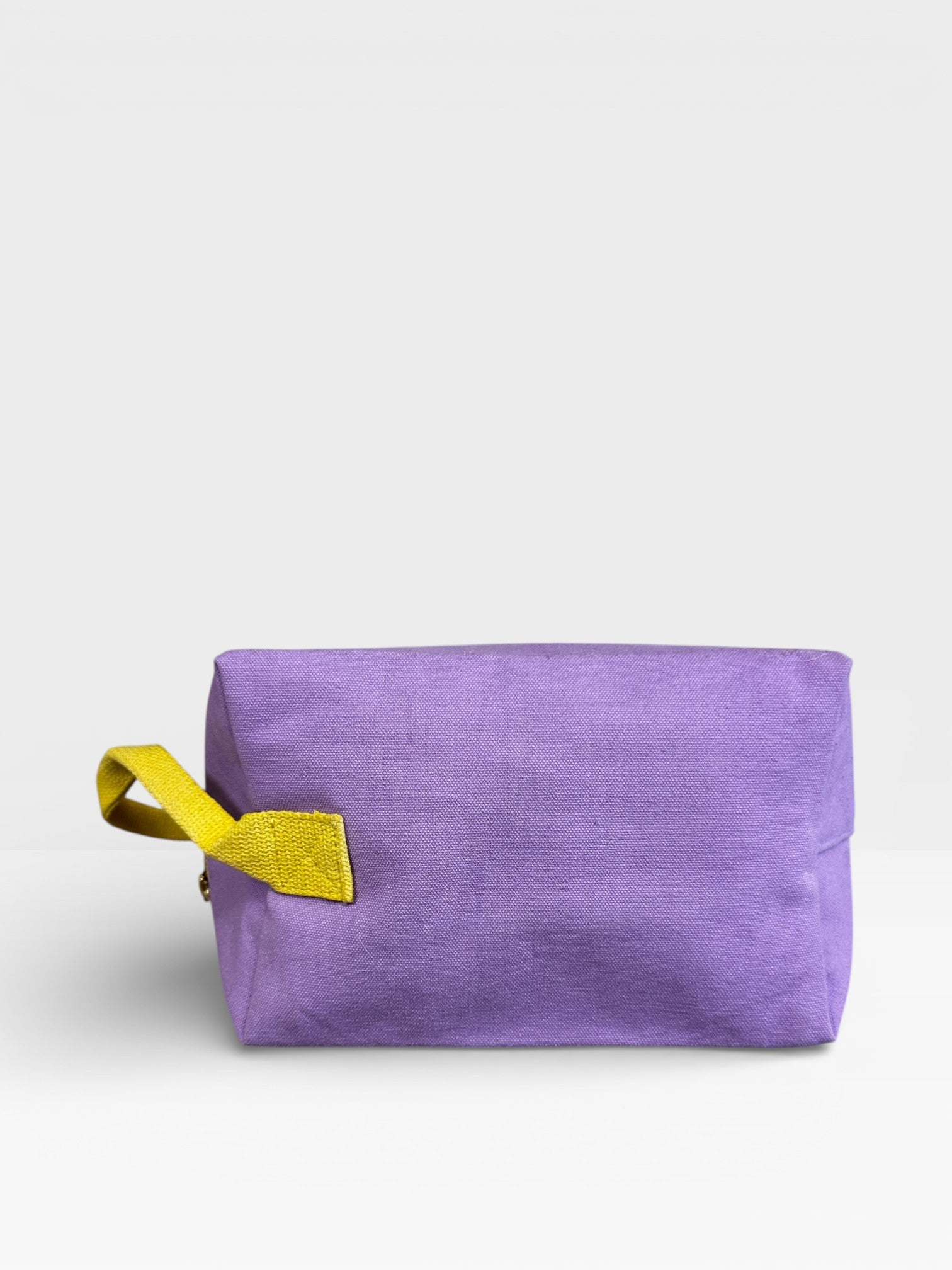Der LEY! Pouch - FLIEDER-GELB von LEY! ist ein rechteckiger, lavendelfarbener Beutel mit einem gelben Tragegriff auf der linken Seite, ideal als Kulturbeutel für Reisen oder für die Mitnahme von Utensilien auf Bauchtaschen Festivals, abgebildet auf einem schlichten weißen Hintergrund.