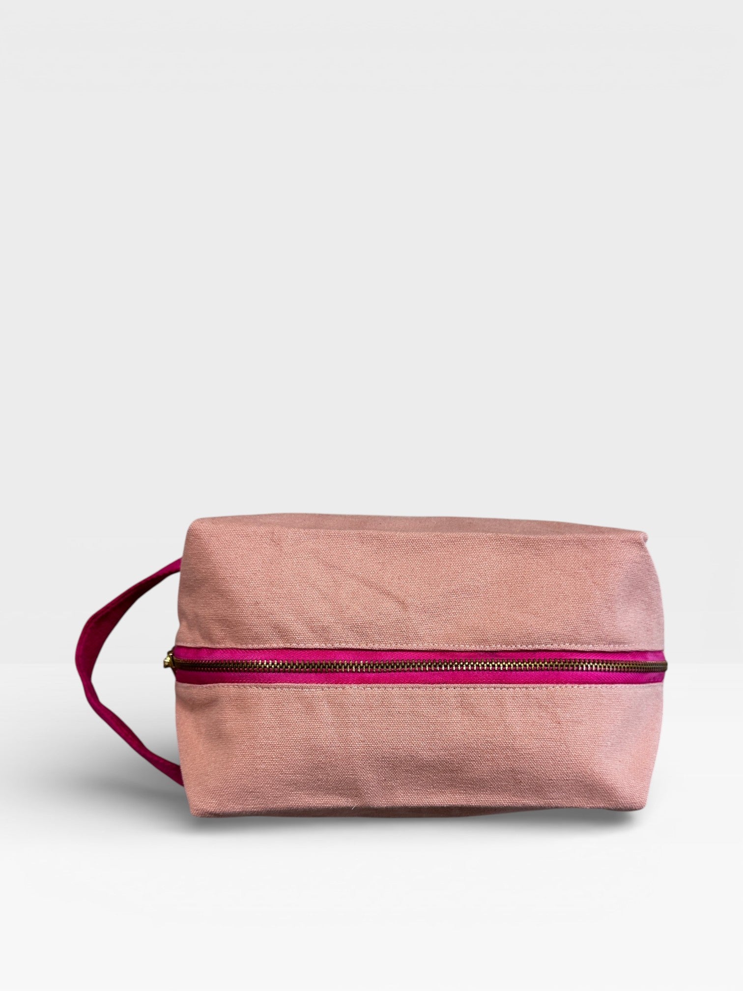 Die LEY! Pouch - NUDE-PINK von LEY! ist ein rechteckiger, rosafarbener Stoffbeutel mit einem magentafarbenen Reißverschluss und einem passenden Henkel an der linken Seite, der sich perfekt als stylisches Festival-Accessoire eignet, abgebildet auf einem schlichten weißen Hintergrund.