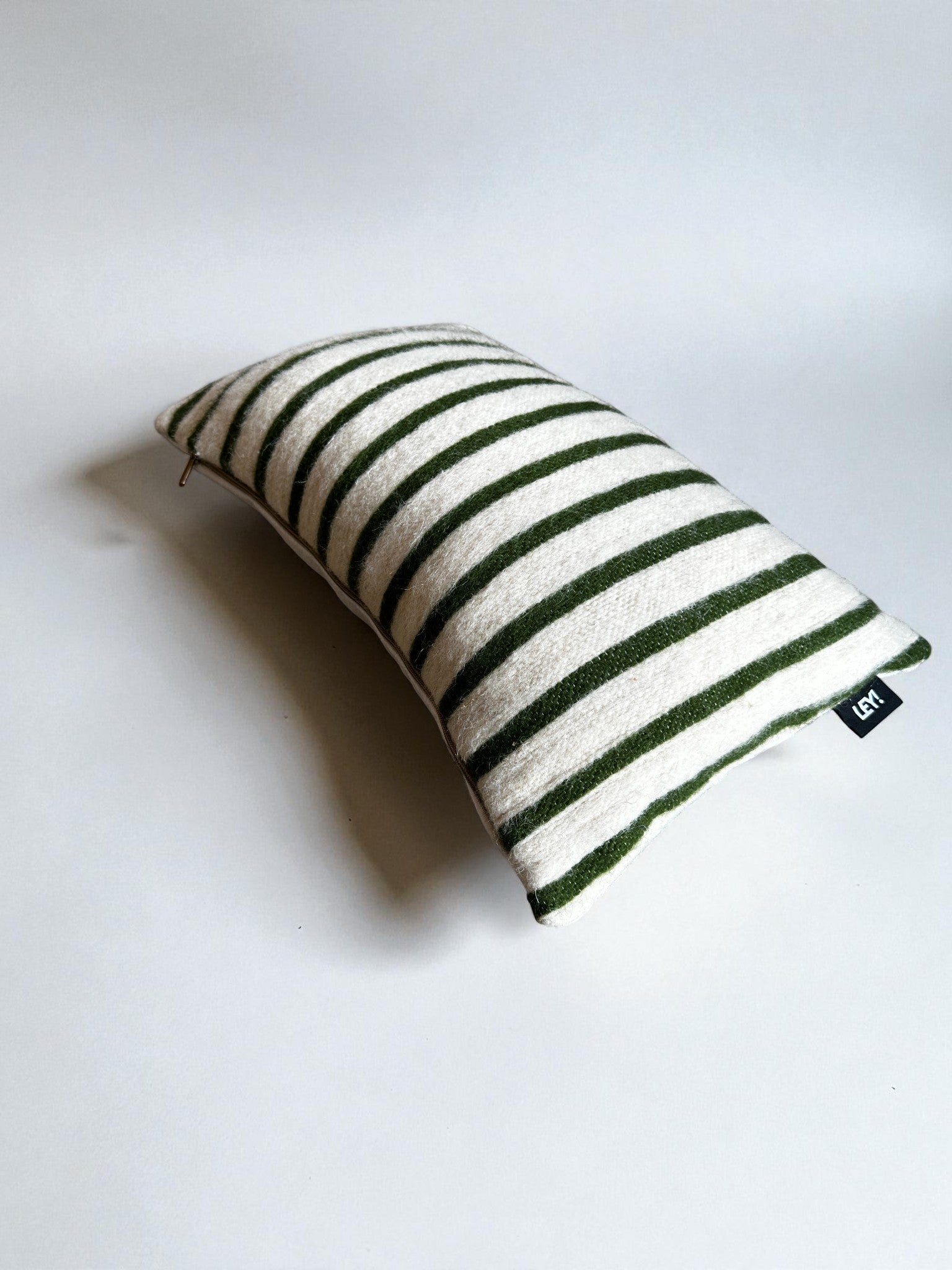 Ein rechteckiges LEY! Kissen - WINTER EDITION - TANNE - 30 x 50 mit grünen und weißen Streifen liegt auf einer schlichten weißen Fläche und trägt ein kleines schwarzes Etikett, das seine handwerkliche Qualität aus Marrakesch unterstreicht.