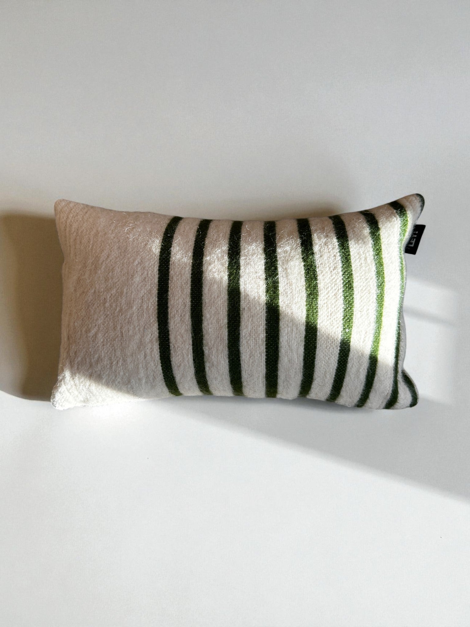 Das LEY! Kissen - WINTER EDITION - TANNE (30 x 50) hat einen weißen Untergrund mit dunkelgrünen vertikalen Streifen und ist auf einer hellen Fläche mit einem Schatten in der Mitte abgebildet.