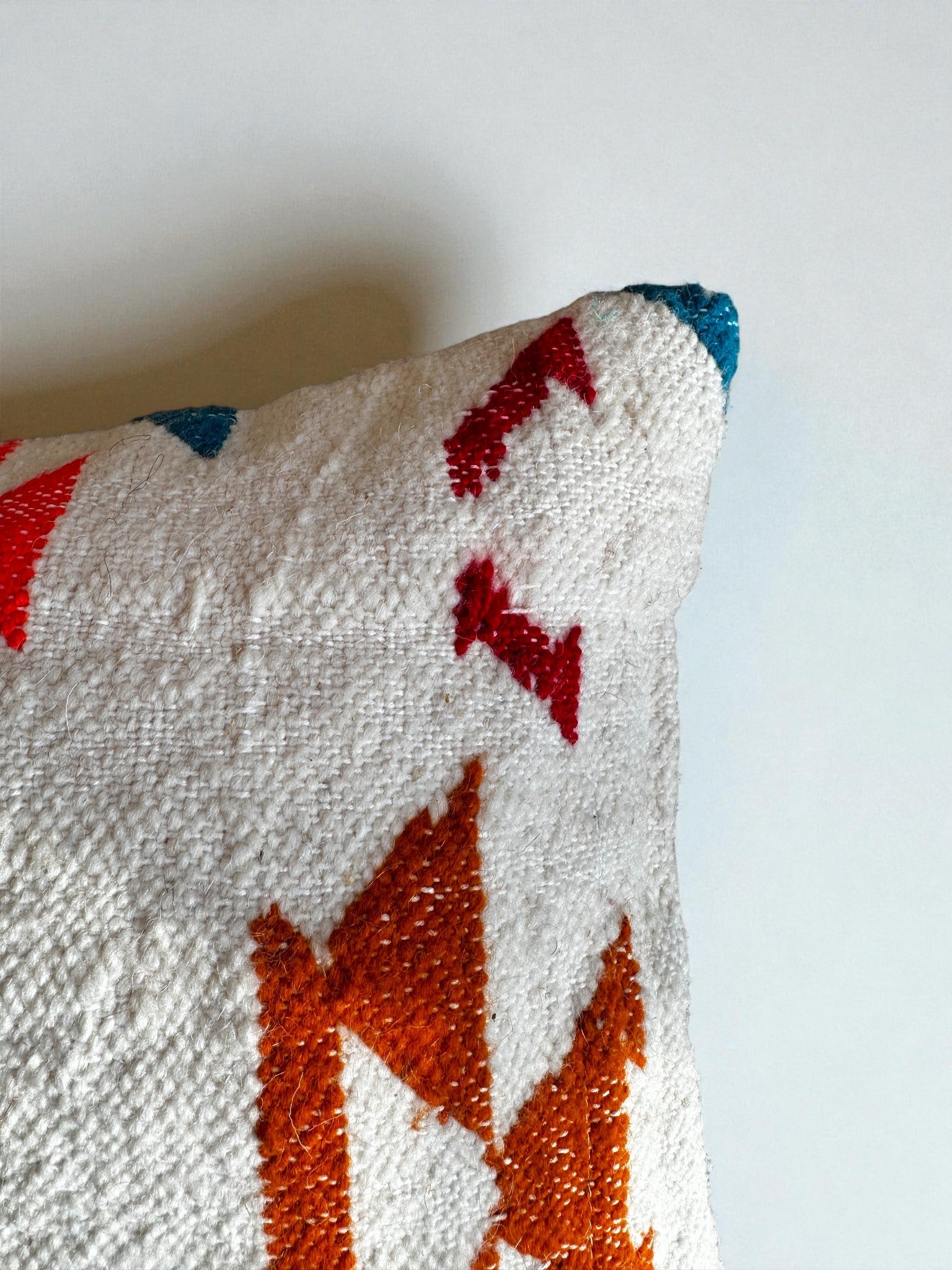 Eine Nahaufnahme des LEY! Kissen - Colorful Line (40 x 60) von LEY! mit weißer strukturierter Schurwolle, roten und orangefarbenen geometrischen Mustern und einem Hauch von Blau oben rechts vor einem schlichten weißen Hintergrund.