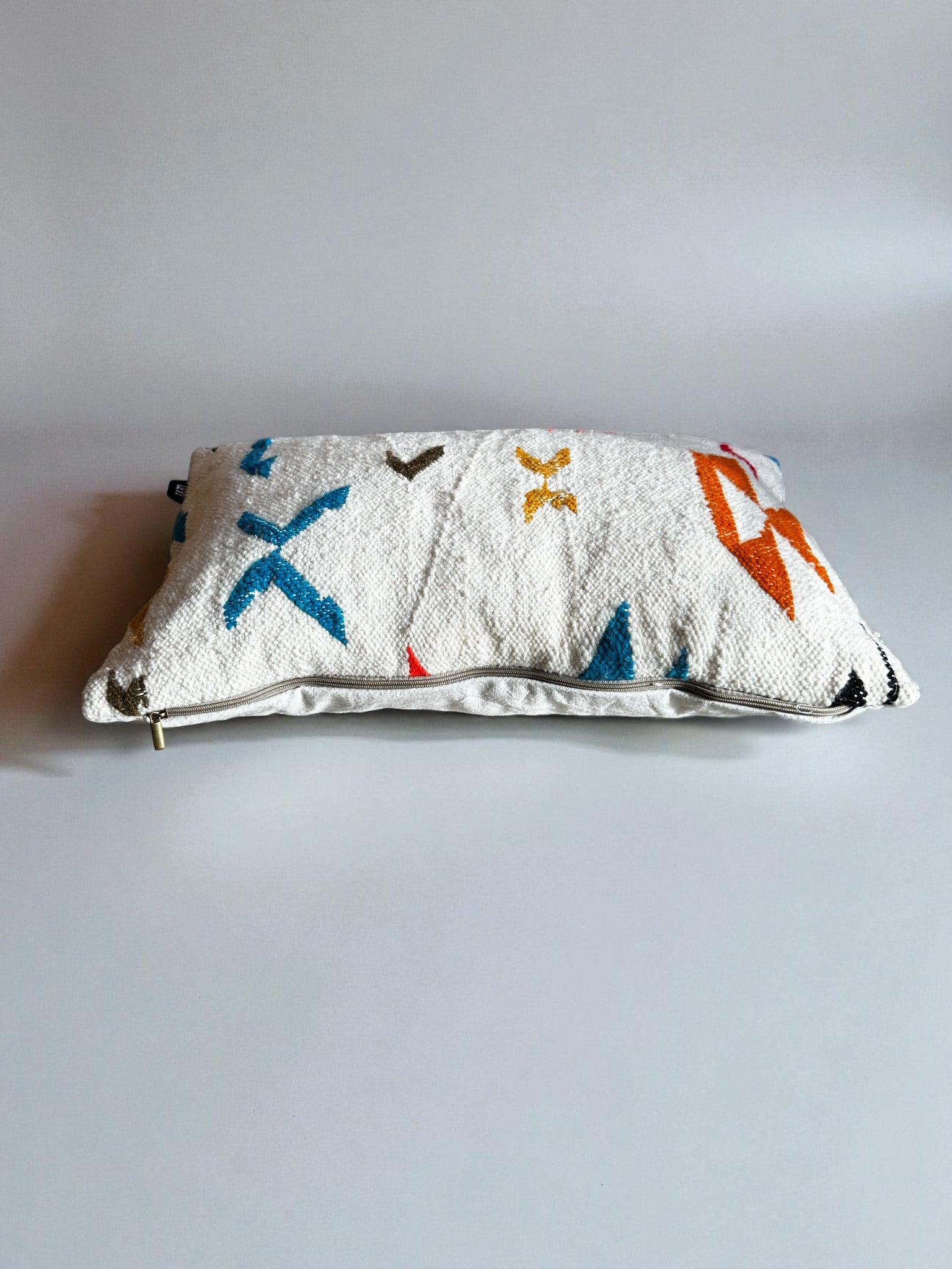 Das LEY! Kissen - Colorful Line (40 x 60), ein rechteckiges, strukturiertes weißes Kissen mit Reißverschluss und abstrakten blauen, orangen, gelben und braunen Formen von LEY!, handgemacht Marrakesch, ruht auf einer schlichten hellgrauen Oberfläche.