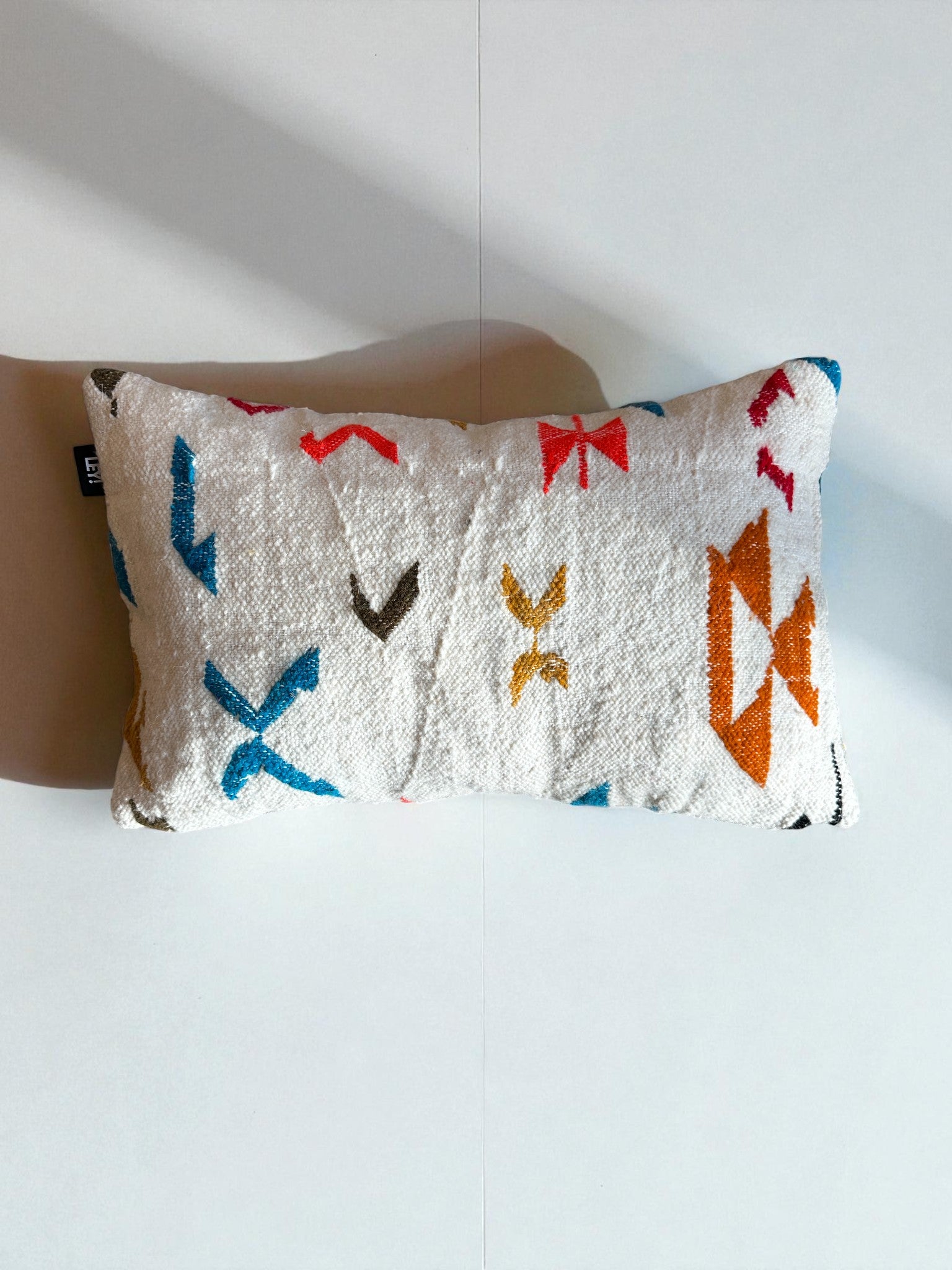 Das LEY! Kissen - Colorful Line - 40 x 60, ein rechteckiges weißes Kissen mit strukturiertem Stoff und abstrakten Mustern in Blau, Rot, Gelb, Orange und Schwarz von LEY!.