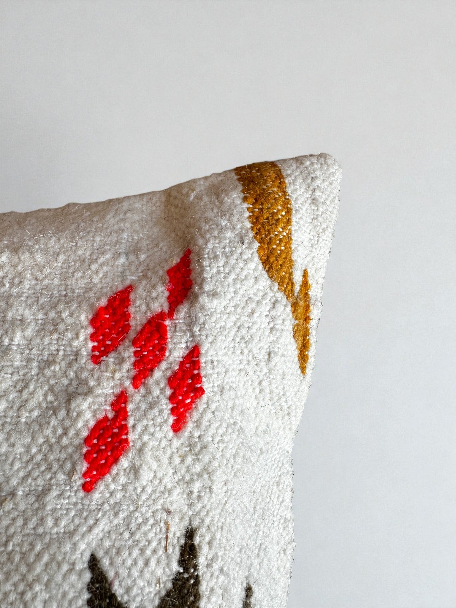 Eine Nahaufnahme des LEY! - Kissen - Colorful Line 40 x 60 von LEY!, mit strukturiertem weißem Stoff mit rotem Rautenmuster, senfgelbem geometrischem Akzent und schwarzem Detail, handgefertigt Marrakesch, auf einfarbigem hellem Hintergrund.
