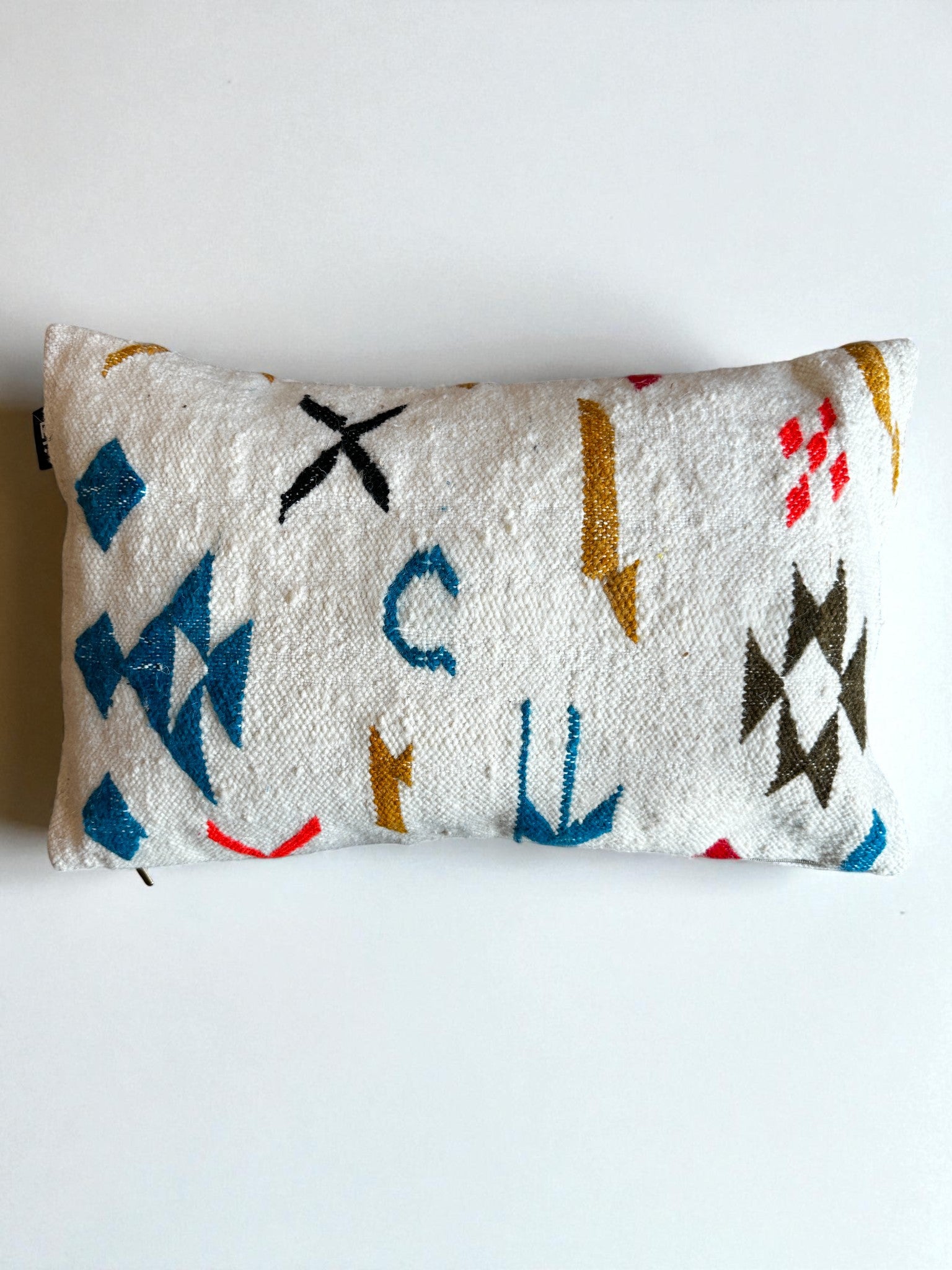 Das LEY! - Kissen - Colorful Line (40 x 60) ist ein rechteckiges, weißes Kissen mit strukturiertem Stoff und leuchtend blauen, gelben, roten und schwarzen geometrischen Mustern, die jedem Raum Handarbeit Marrakesch-Flair verleihen. Marke: LEY. Einfarbig weißer Hintergrund.