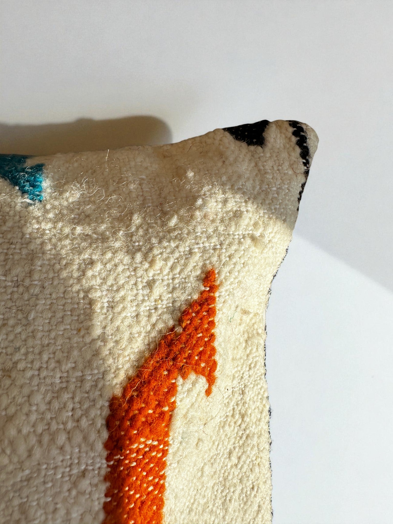 Nahaufnahme des LEY! Kissen - Colorful Line (40 x 60) von LEY! mit strukturierter, cremefarbener Oberfläche, orangefarbenem Pfeilmuster, dezenten schwarzen und blauen Akzenten und Marrakesch-Handwerk auf weißem Hintergrund.