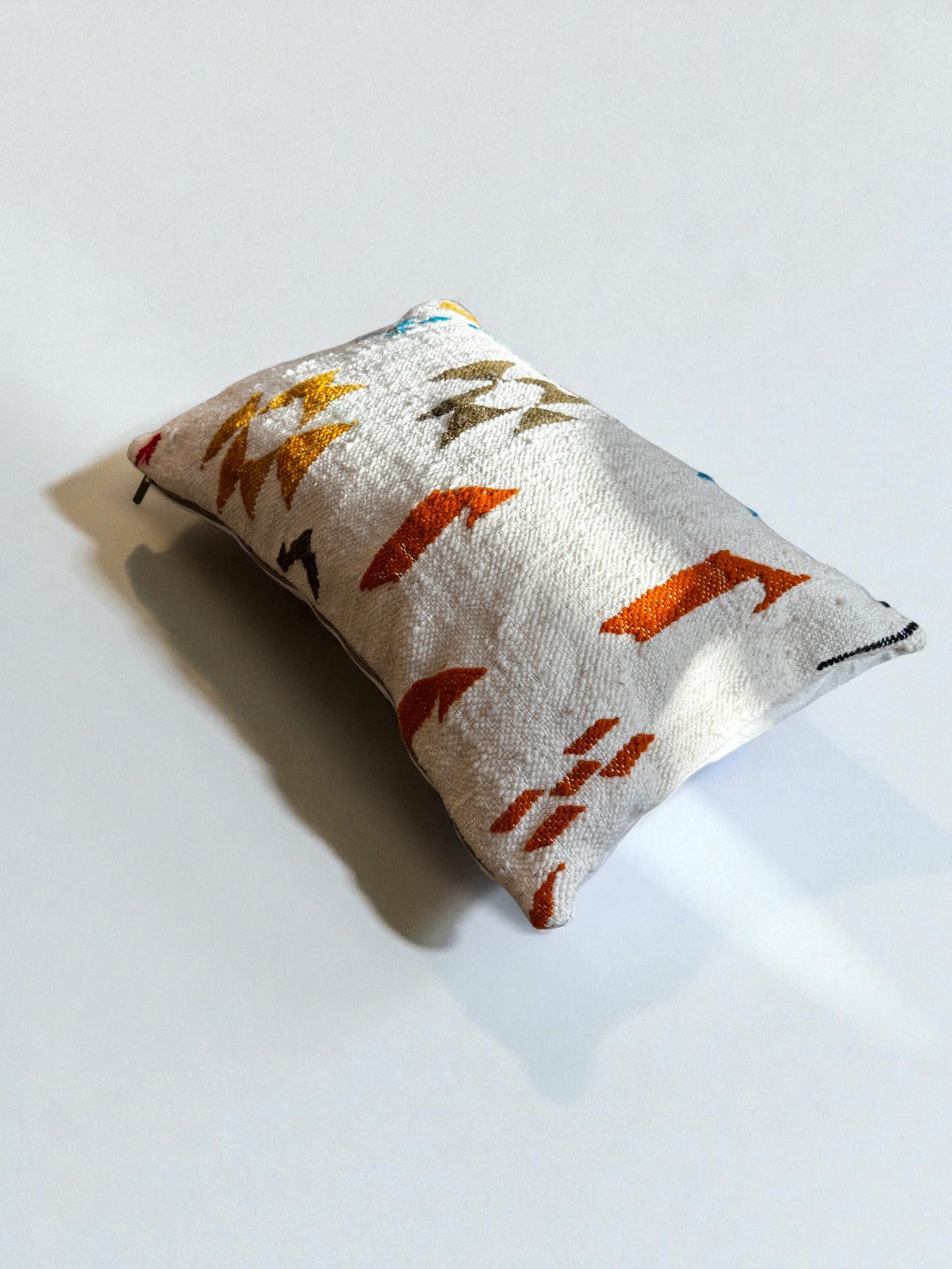 Das LEY! - Kissen - Colorful Line (40 x 60) von LEY! ist ein rechteckiges Dekokissen mit weißem Stoff und lebhaften geometrischen Mustern, die elegant auf einer schlichten weißen Fläche präsentiert werden.